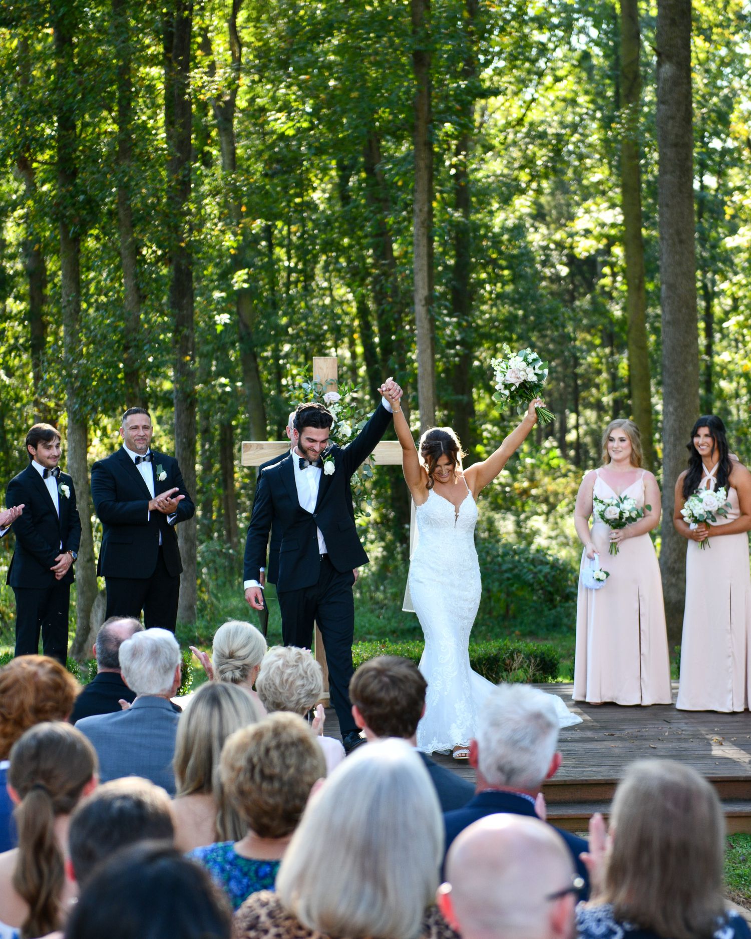 A celebratory moment during an outdoor forest wedding ceremony with guests watching.