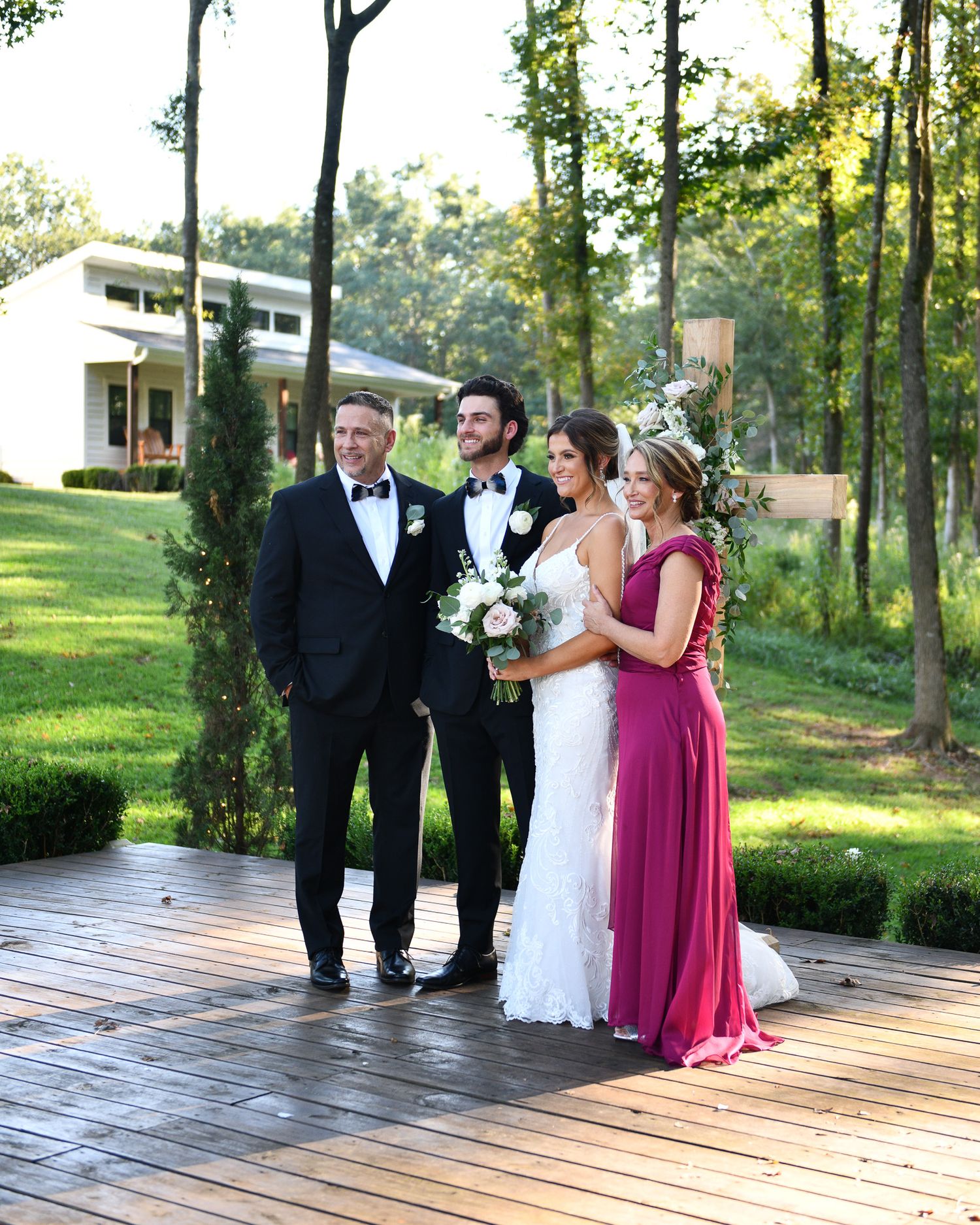 Wedding party posing on wooden deck with lush green forest backdrop.