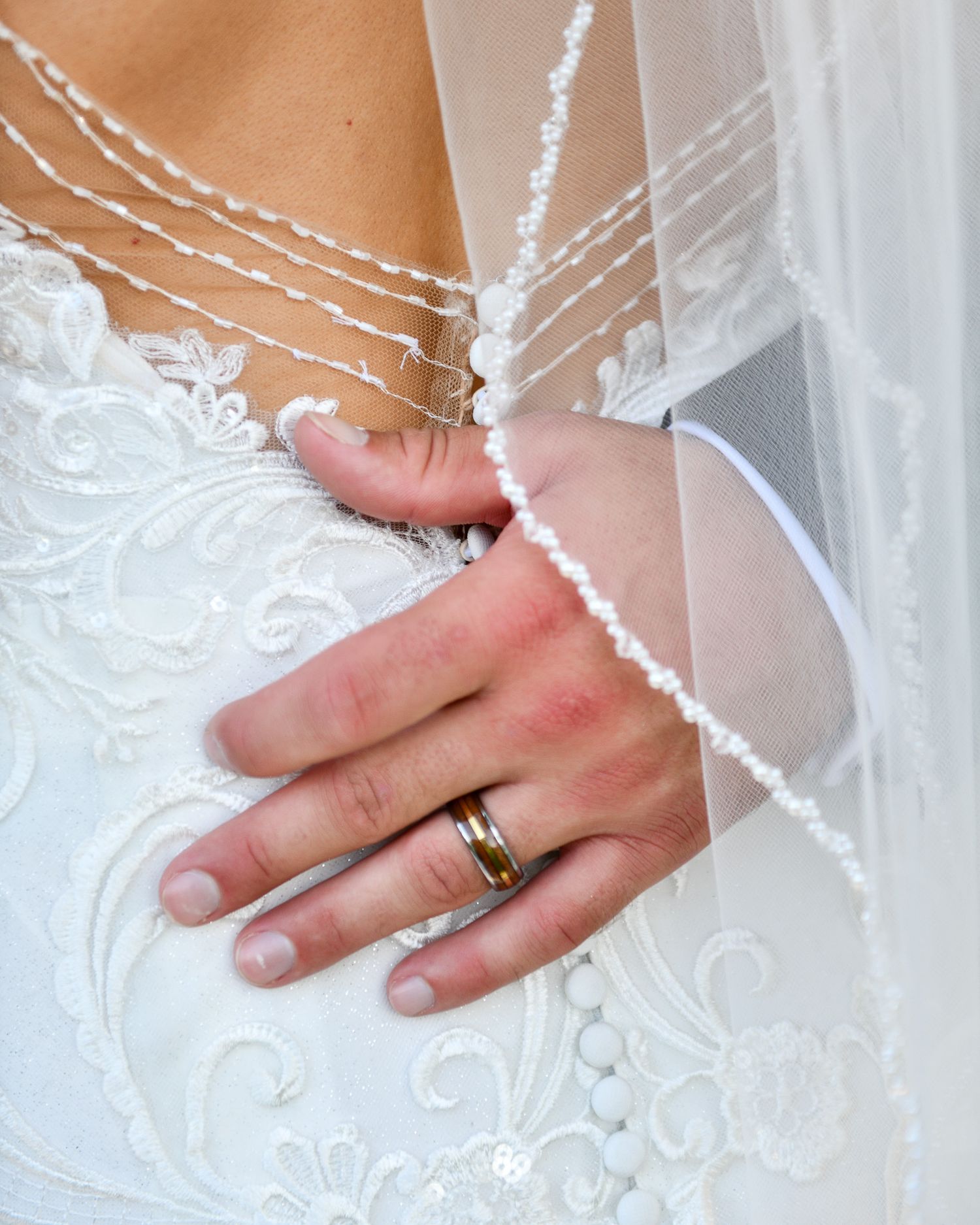 Close-up of a wedding ring and delicate lace veil details on a white dress.