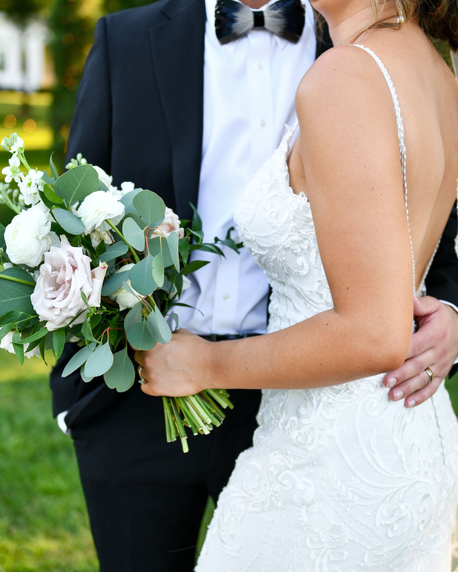 A wedding couple embraces while holding a romantic bouquet of white roses and eucalyptus.