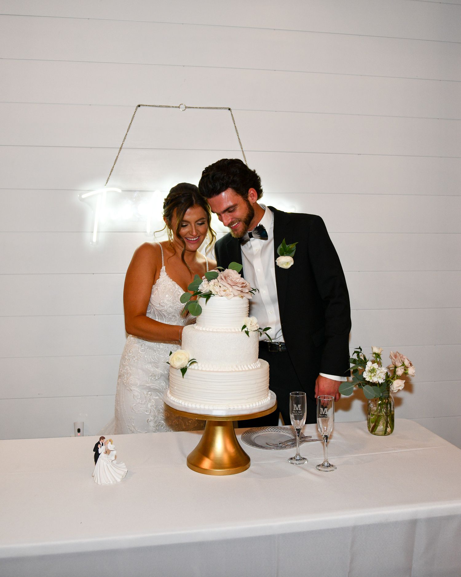 Elegant white wedding cake on gold stand with floral accents at reception.