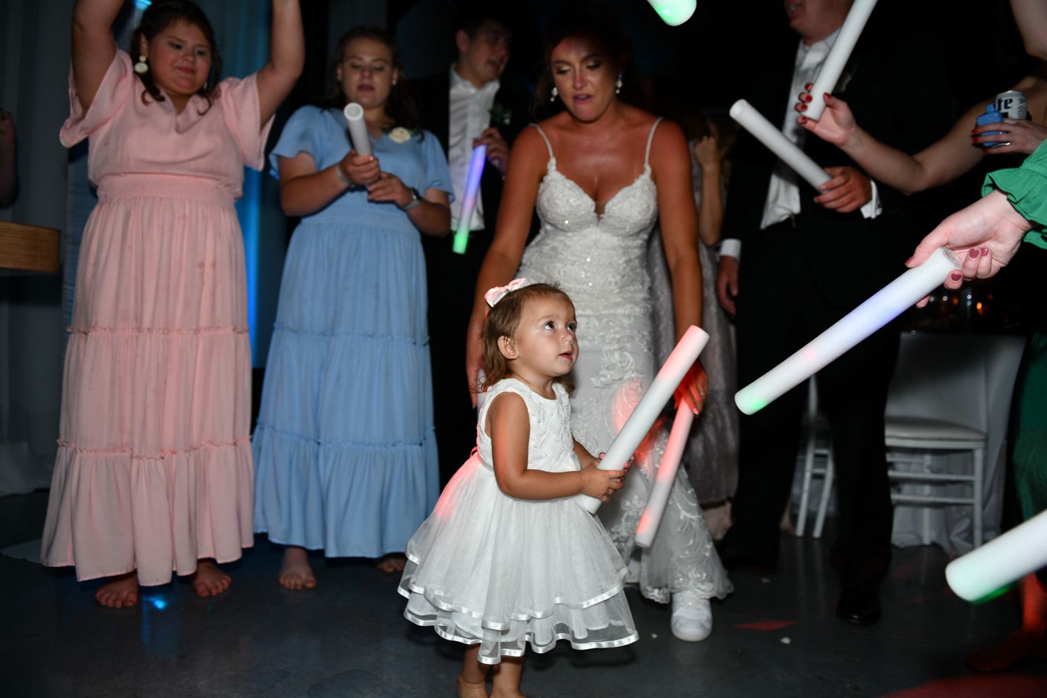Wedding reception scene with guests in pastel dresses and glowing light sticks.