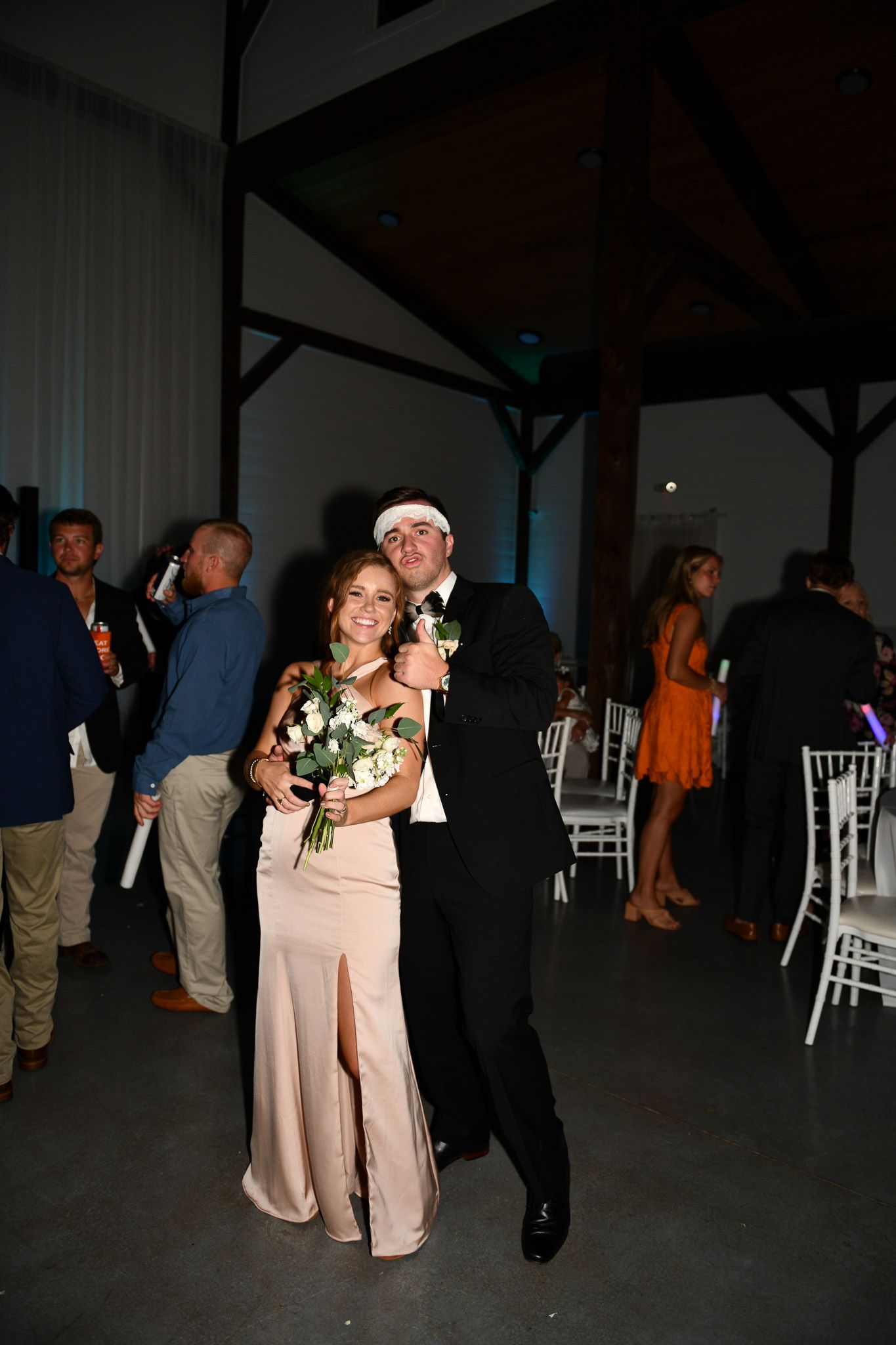 Evening wedding reception with guests mingling among white chairs and dim lighting.