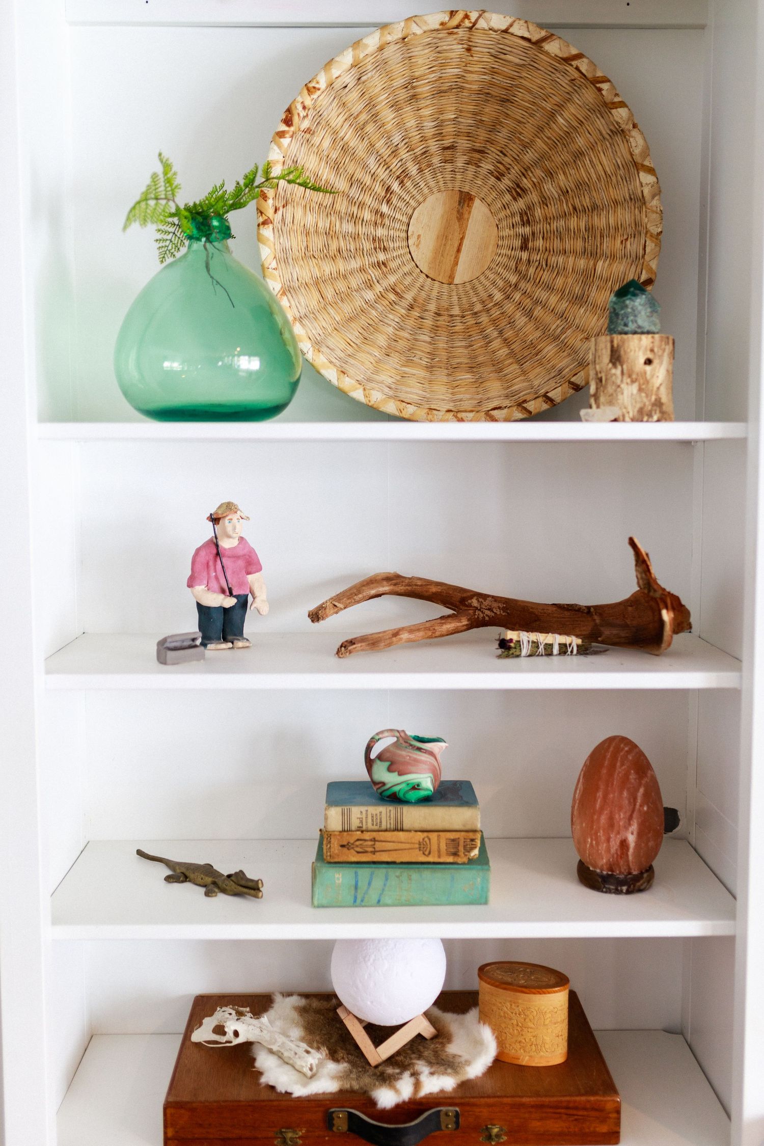 Decorative shelf display with woven basket, green vase, vintage books and coastal accents.