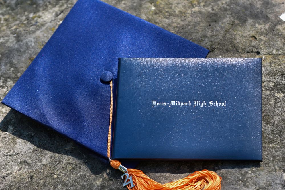 Blue graduation cap with orange tassel lying on stone surface.