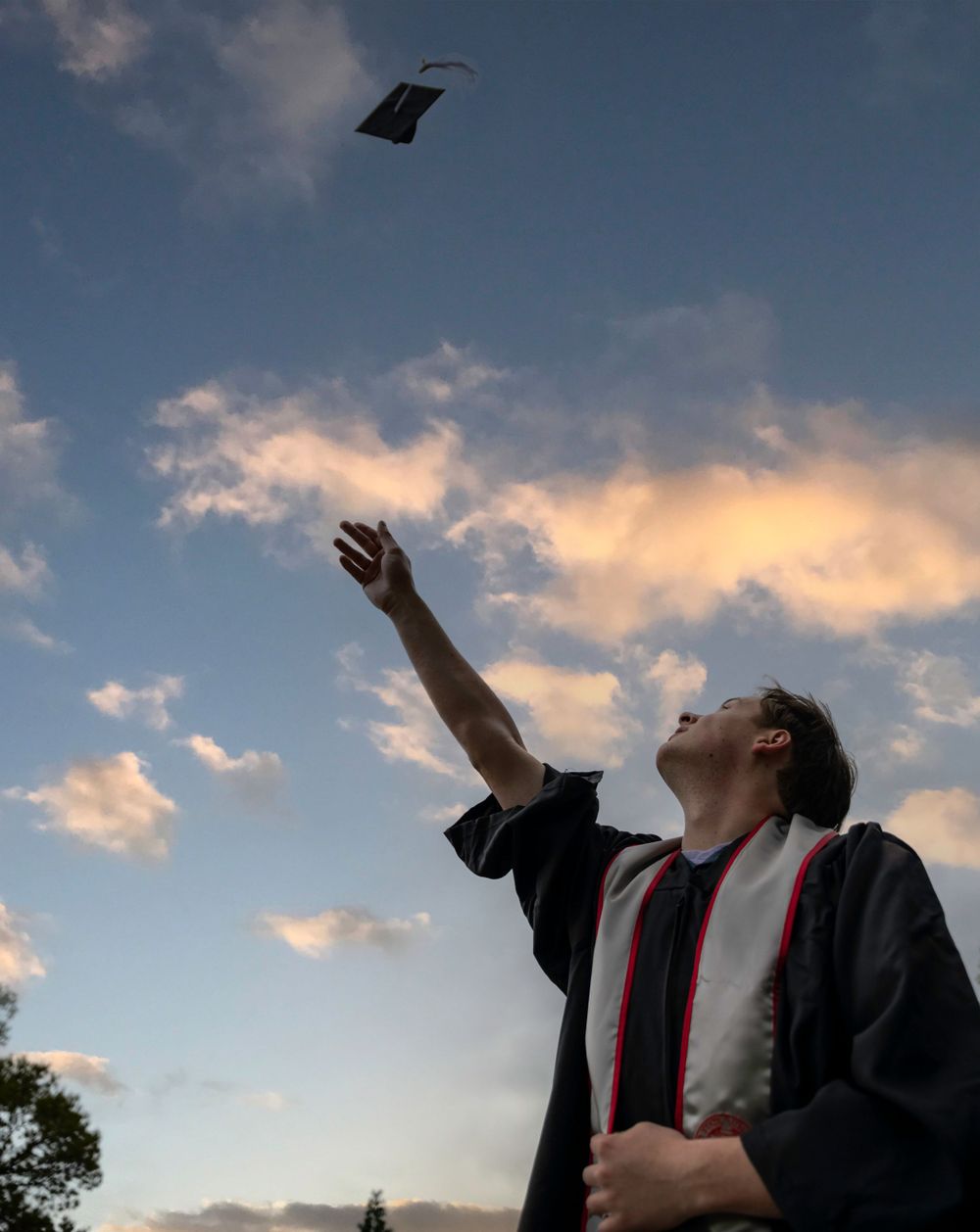 Silhouette of graduate throwing cap in air against sunset sky during graduation celebration.