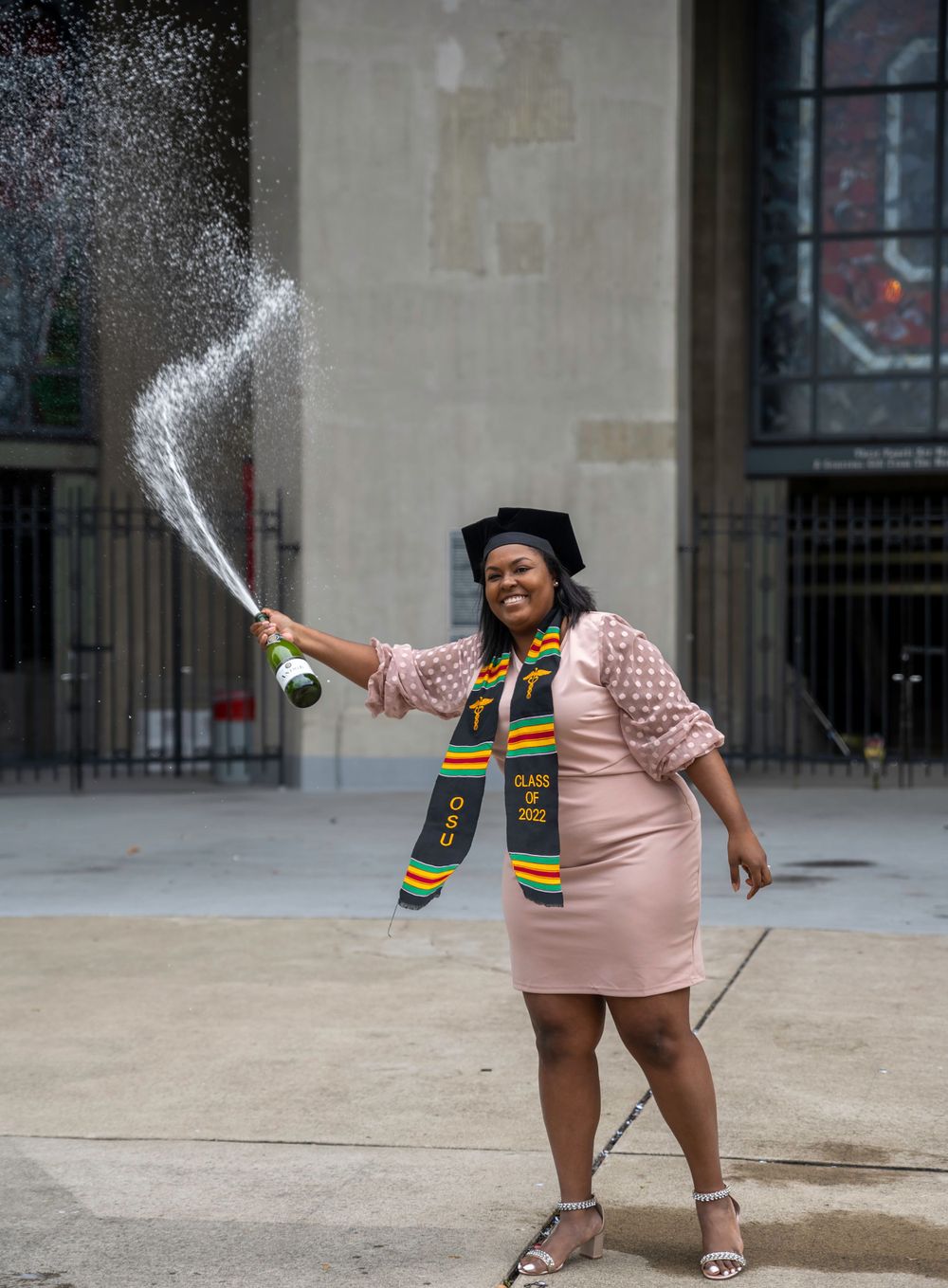 Graduate celebrating by spraying champagne while wearing cap and gown.