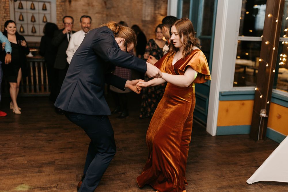 Wedding guest in orange velvet dress dancing energetically with partner at reception.