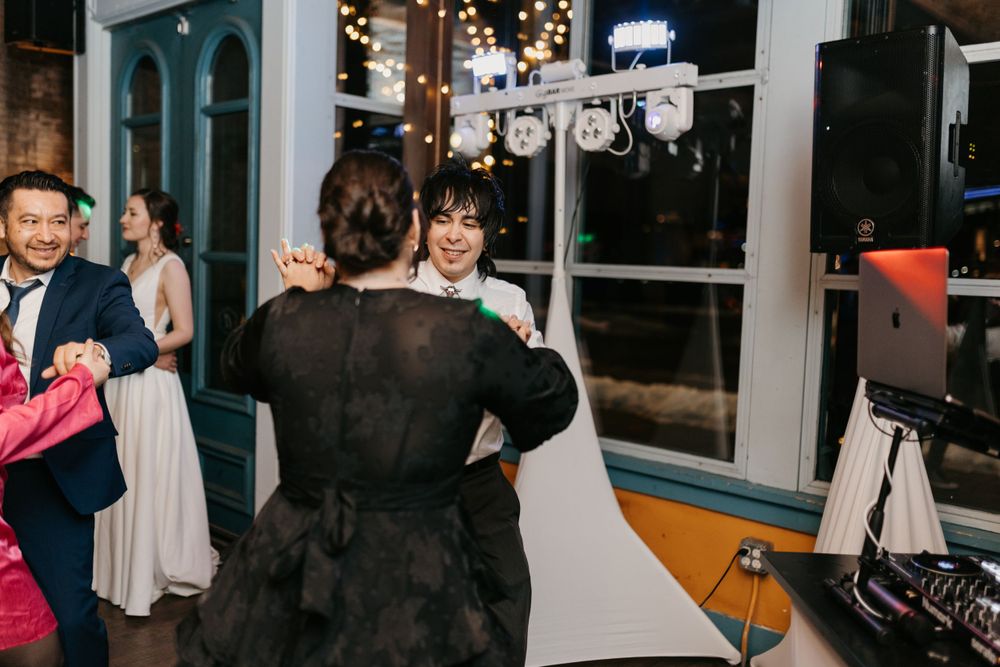 Wedding guests dancing near DJ booth with string lights at festive reception.