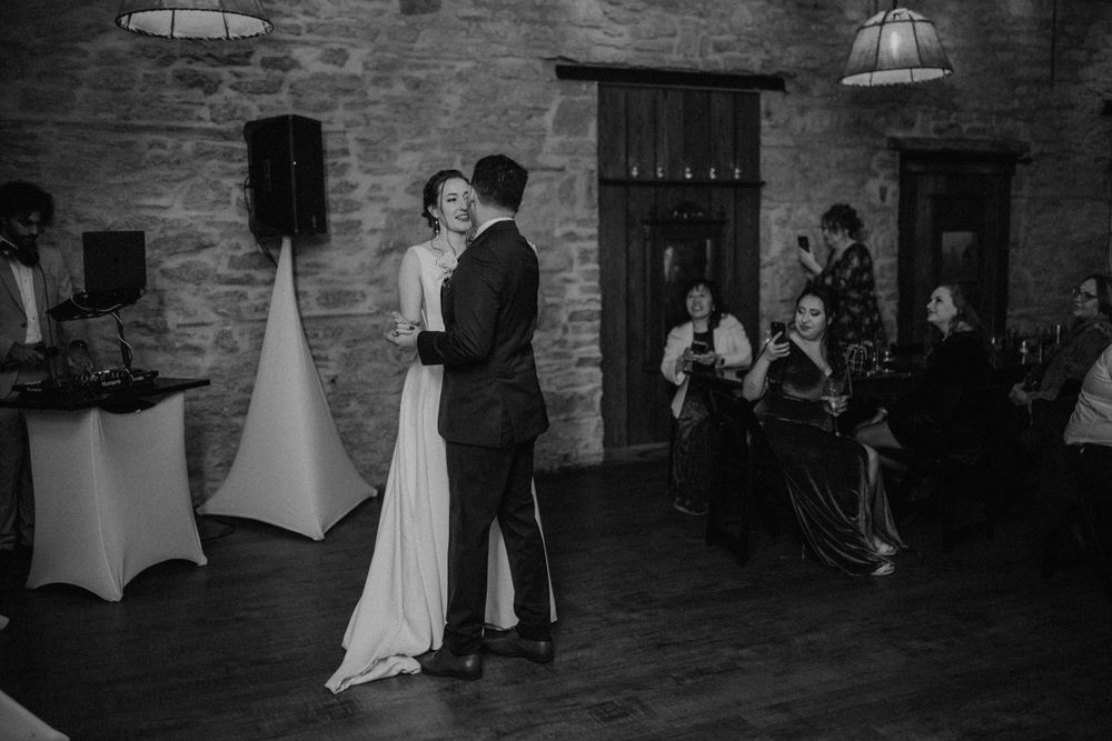 Black and white photo of bride and groom sharing first dance in a rustic stone wedding venue.