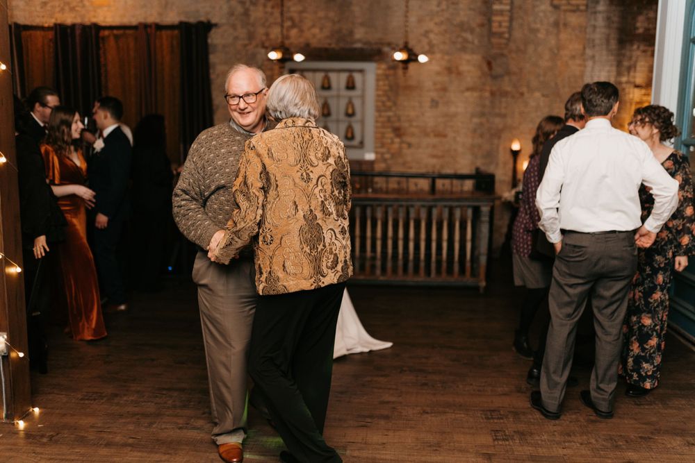 Elderly couple dancing together at rustic wedding reception with warm candlelit stone walls.