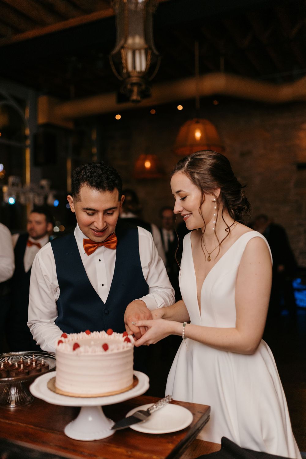 Bride and groom cutting elegant white wedding cake together at rustic reception venue.