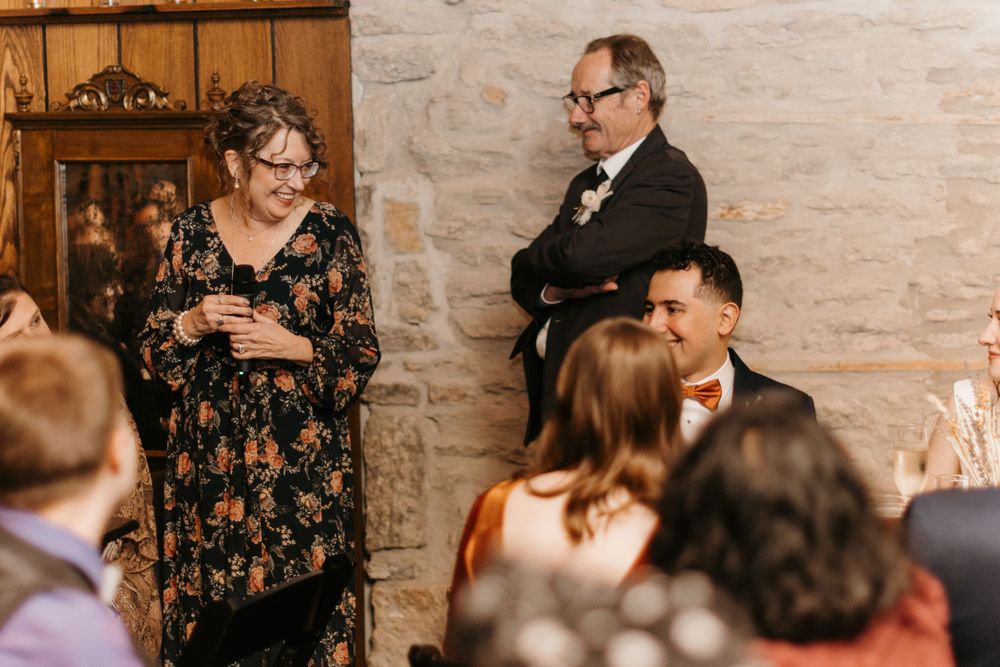 A woman in a floral dress smiles while holding a drink at an elegant wedding reception in a stone venue.