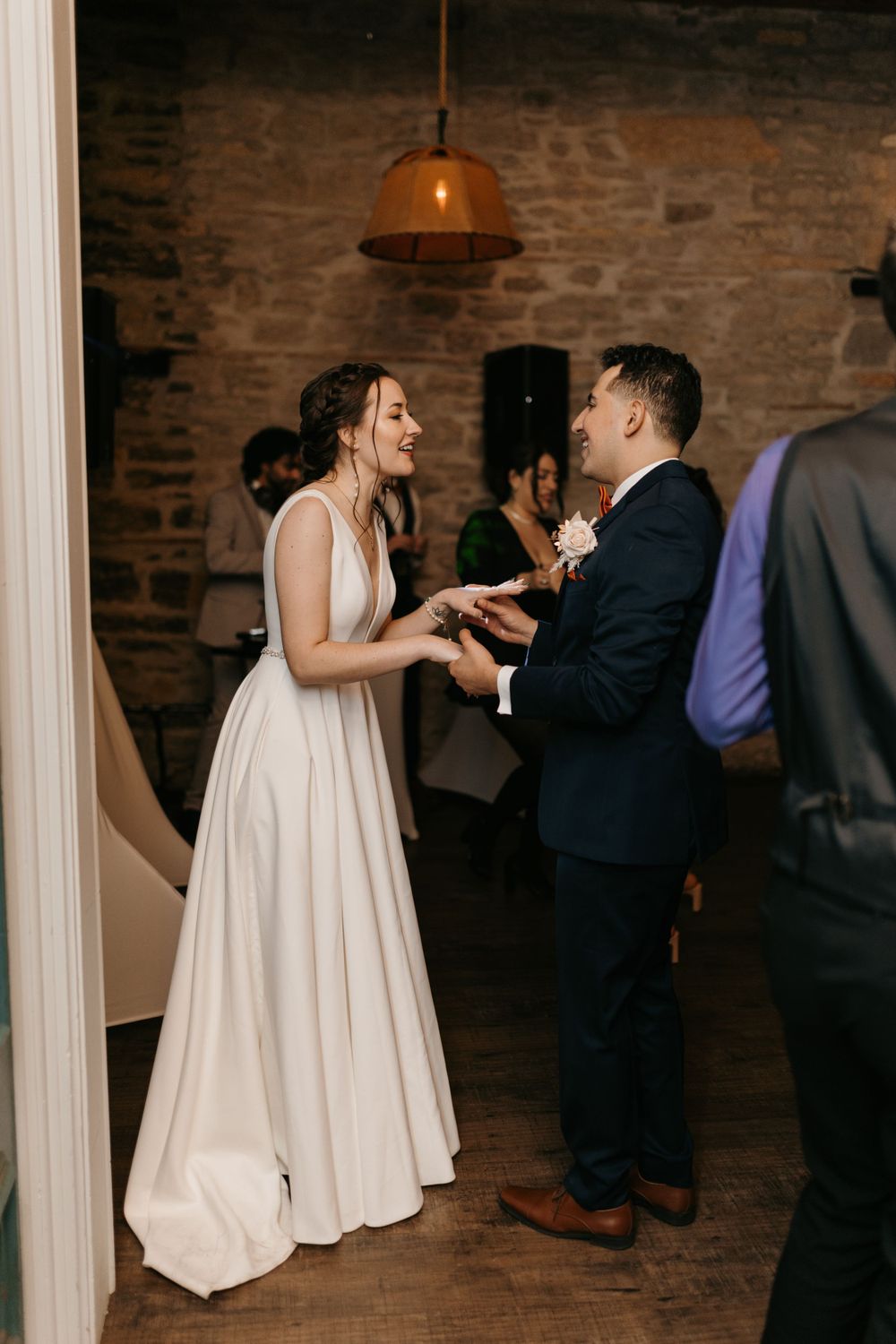Bride and groom share a joyful moment holding hands in rustic stone-walled wedding venue.