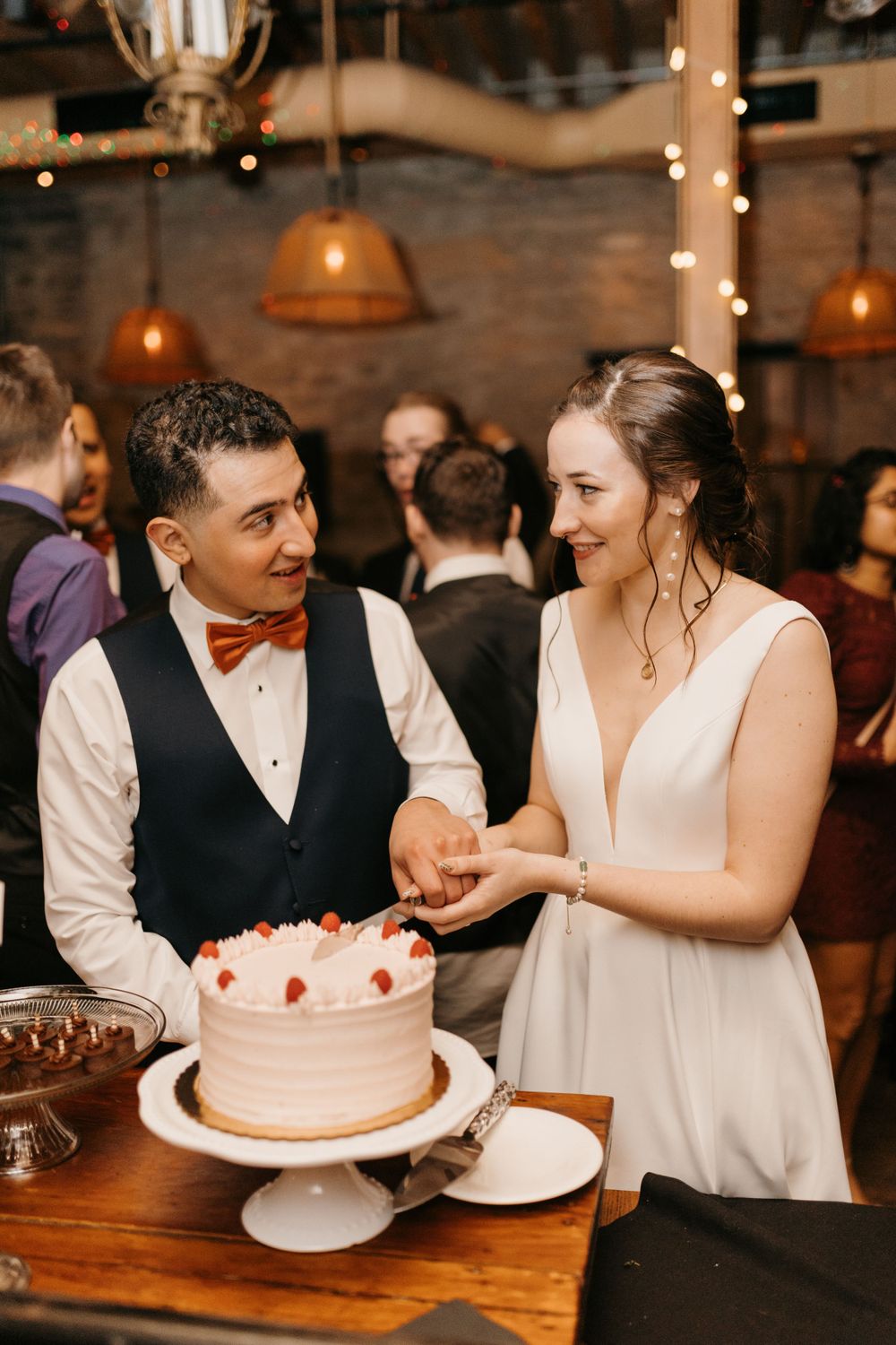 Bride and groom smiling while cutting white wedding cake decorated with strawberries.