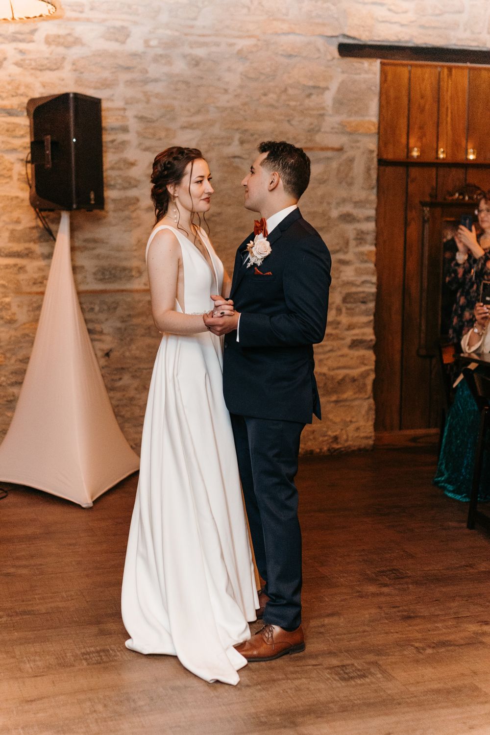 Bride and groom smile at each other during their first dance in a beautiful stone wedding venue.