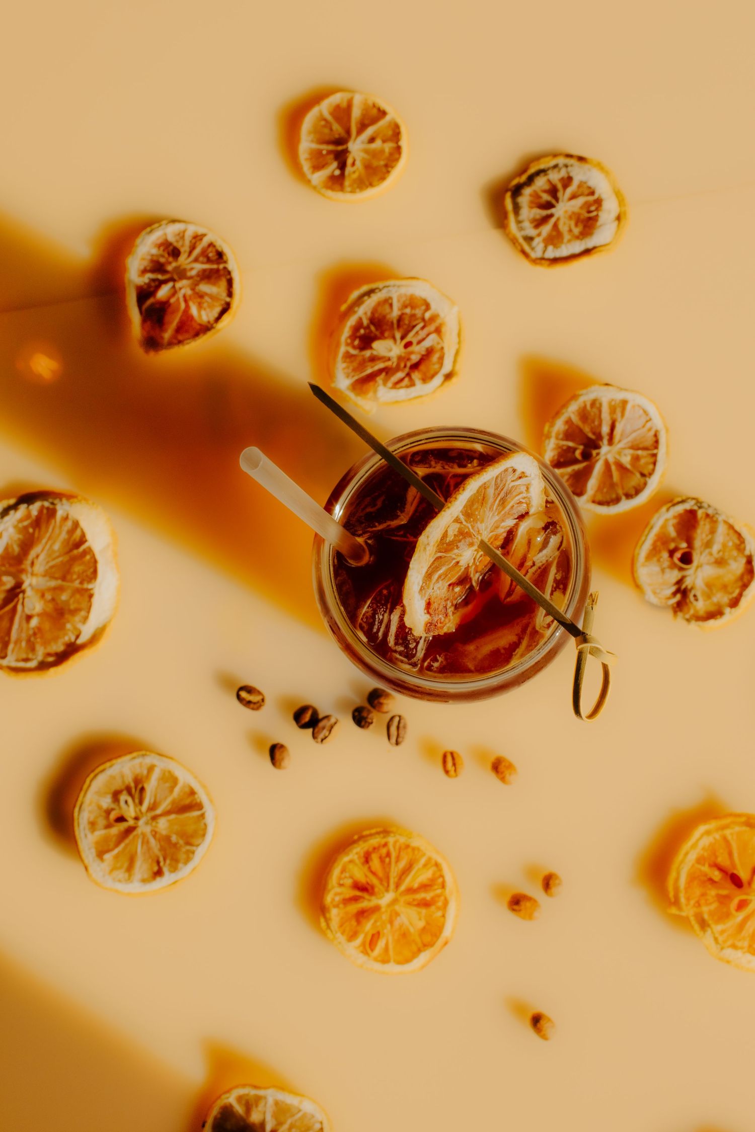 Overhead view of dried orange slices and cocktail drink on warm-toned background.