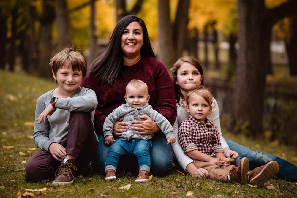 Mother sitting on autumn grass with four young children surrounded by fall foliage.