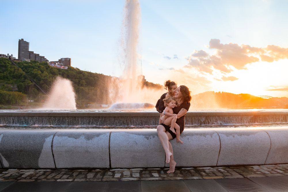 Couple embracing romantically at sunset near large fountain in city park.