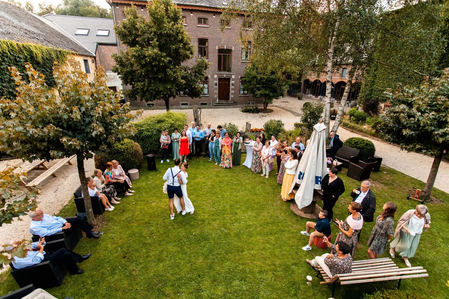 Aerial view of wedding guests gathered on a manicured lawn during an outdoor ceremony.