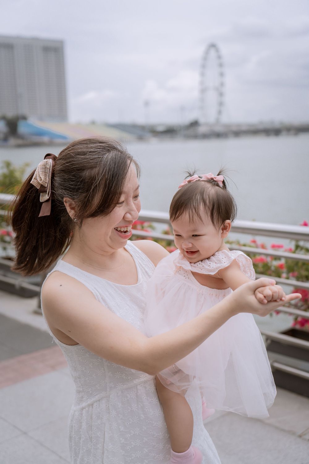 Parent and baby sharing laughs at Singapore's waterfront with Ferris wheel visible.