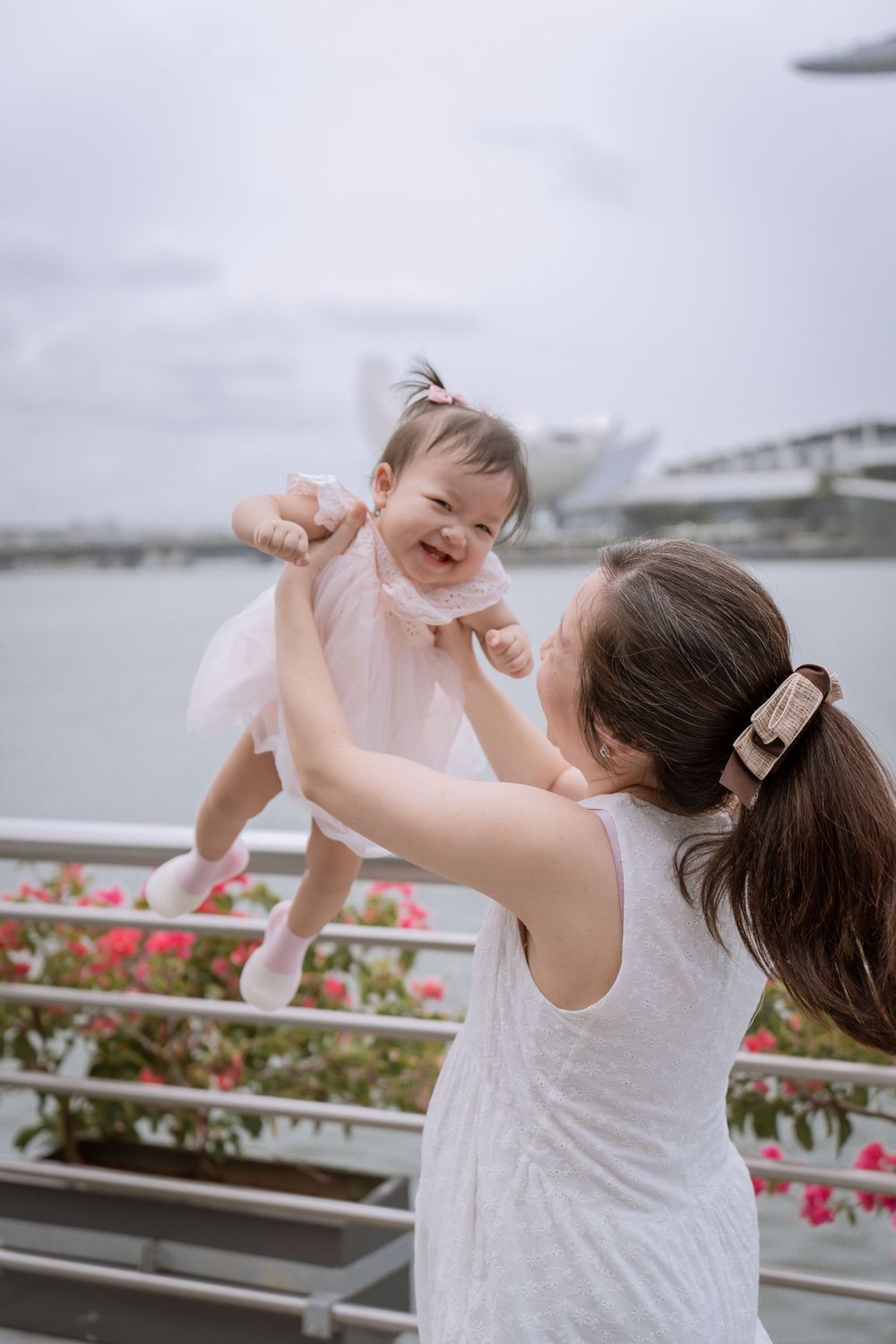 Parent lifting giggling baby against Singapore's iconic waterfront backdrop.