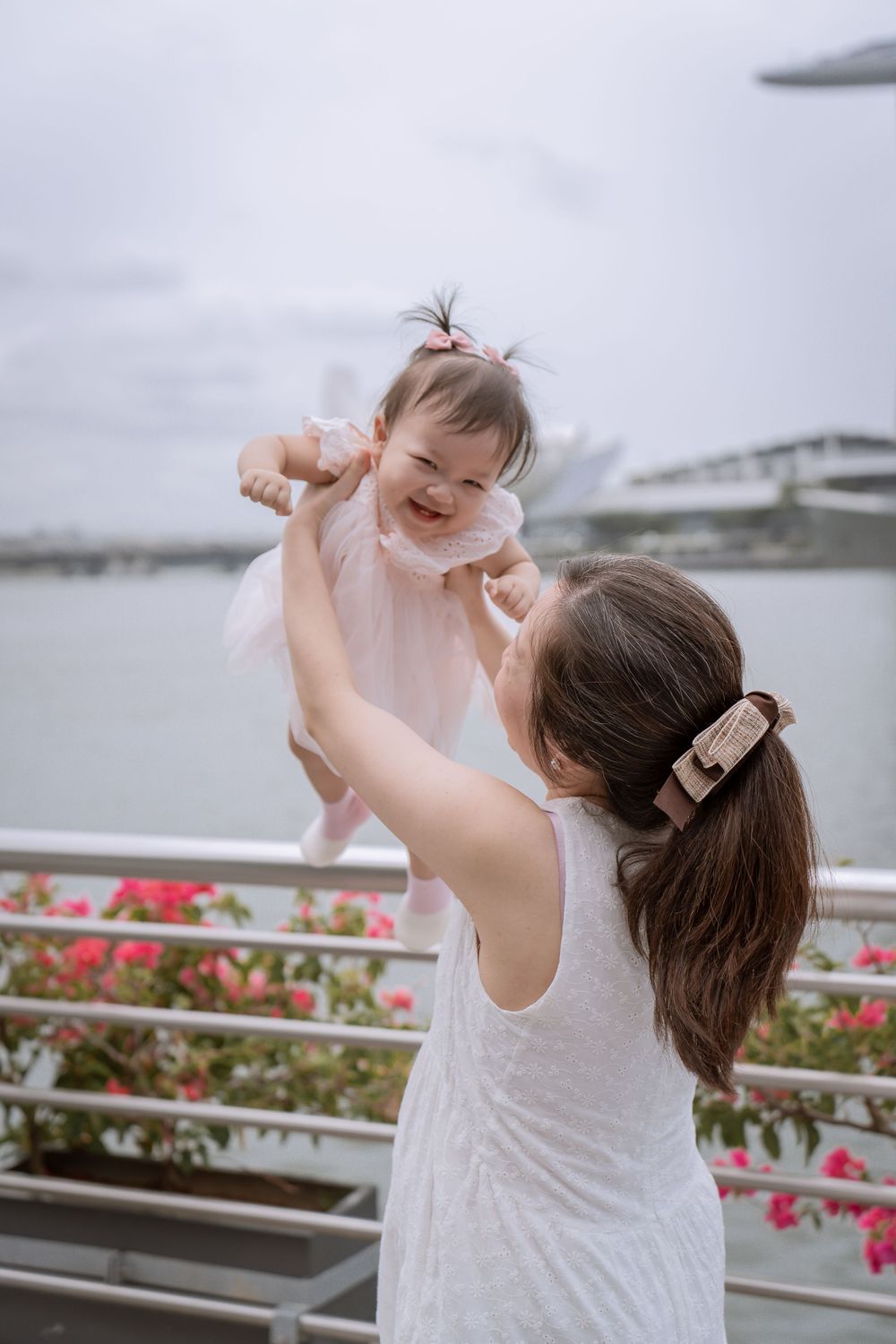 Parent lifting happy baby in pink dress with Marina Bay Sands backdrop.