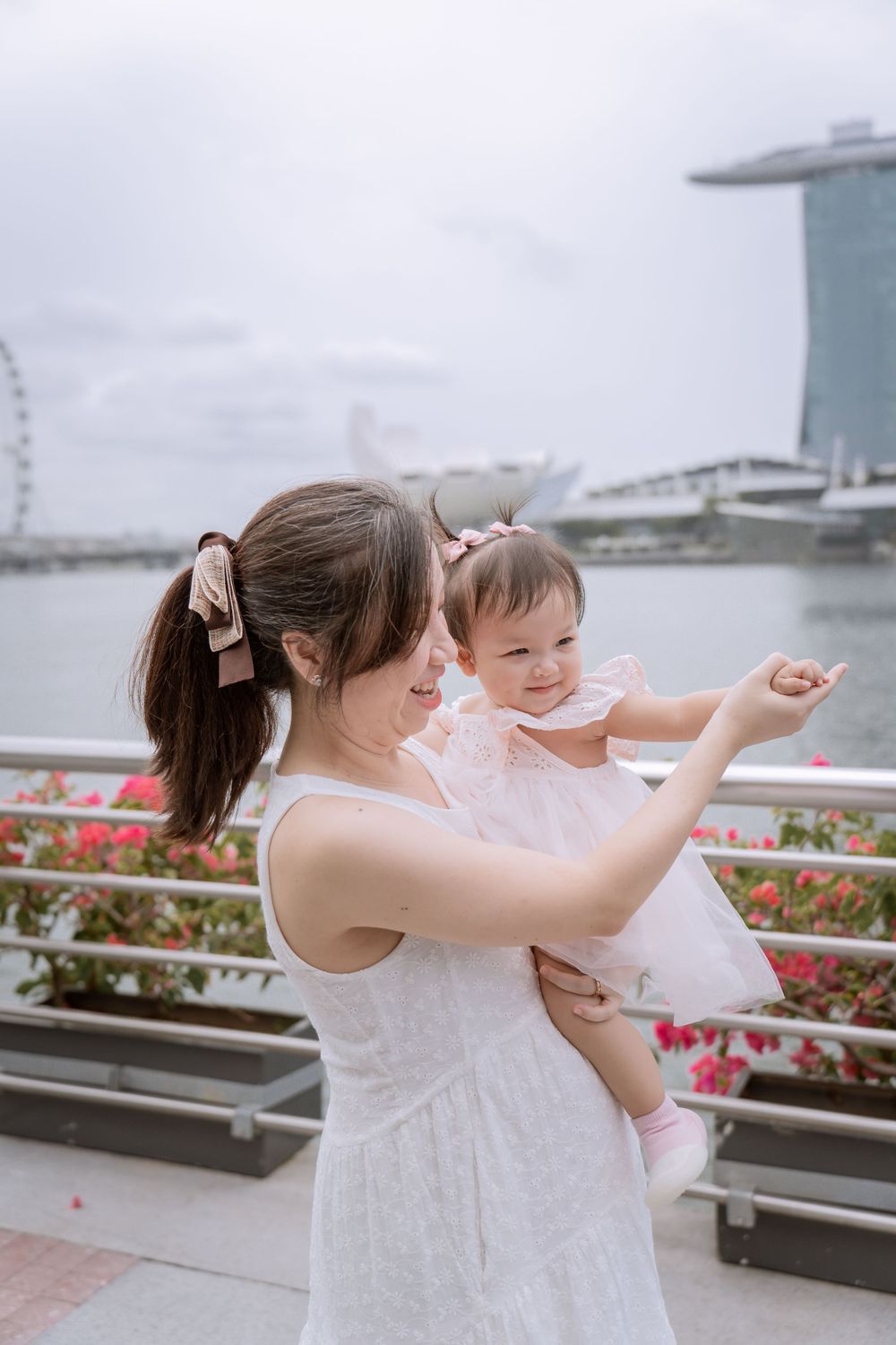 Parent and baby in white dresses enjoying Marina Bay waterfront views.