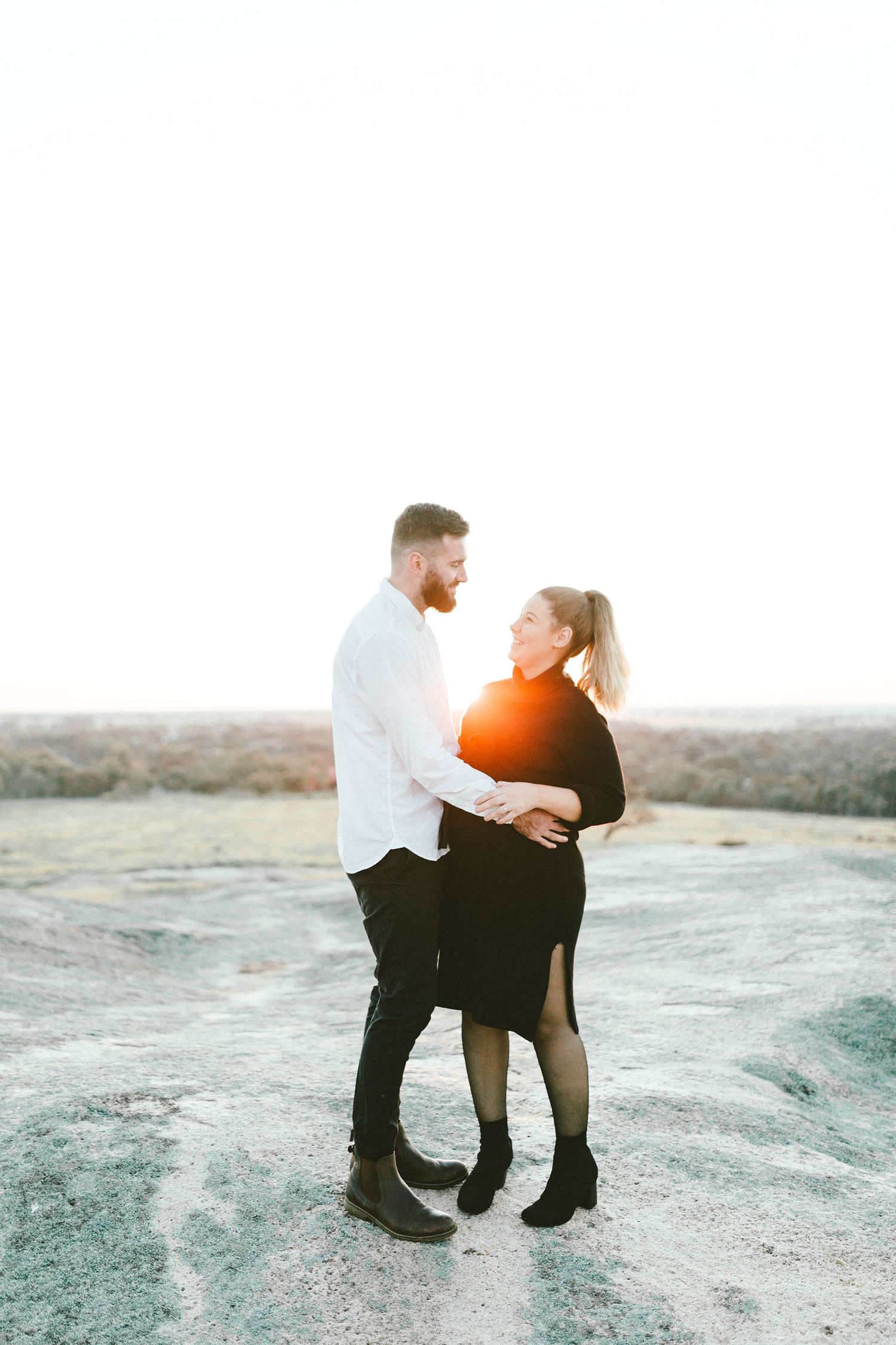 A couple embraces on a rocky surface during a sunset photoshoot.