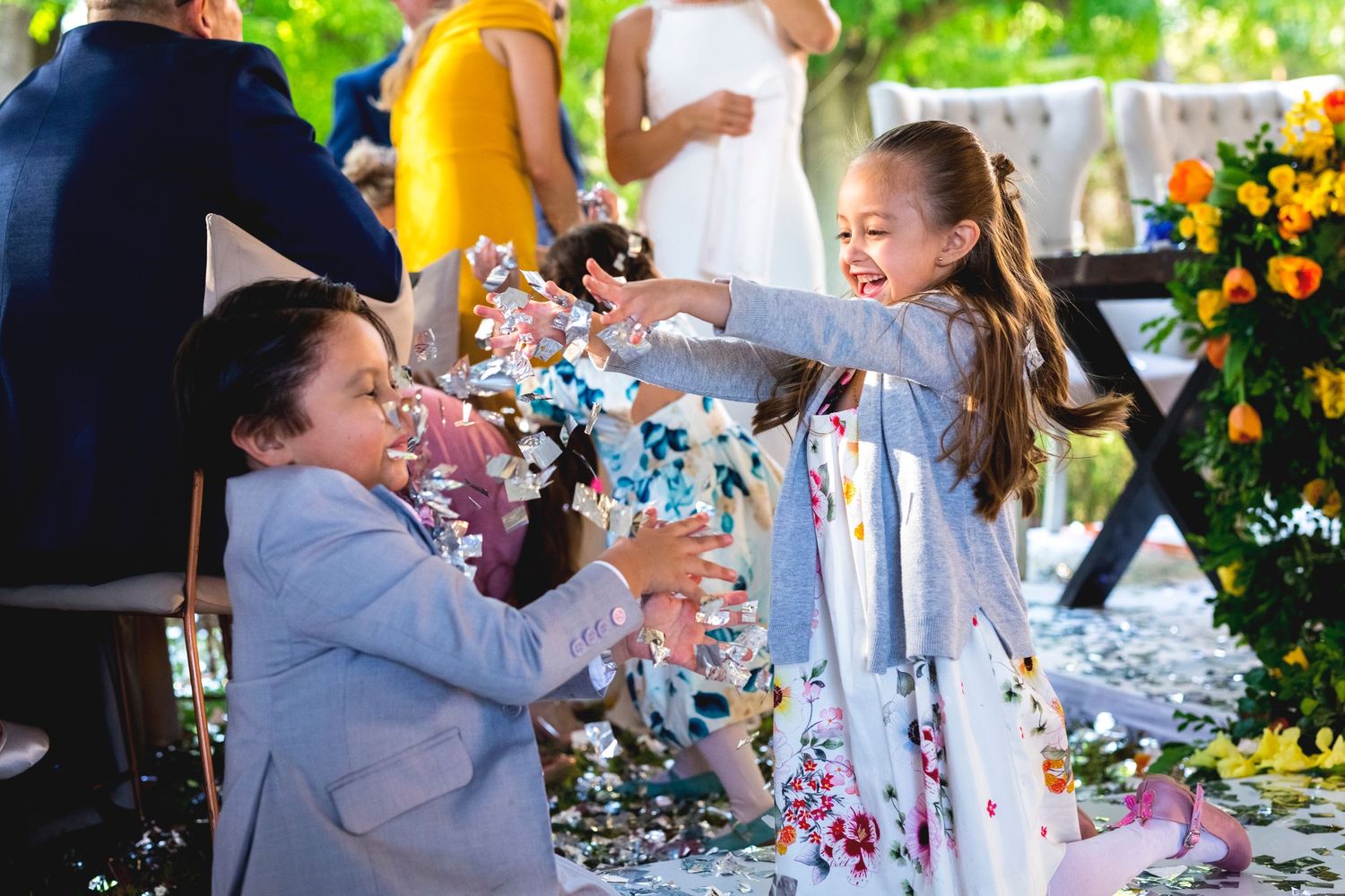 Children playing with confetti at an outdoor wedding celebration with floral decorations.