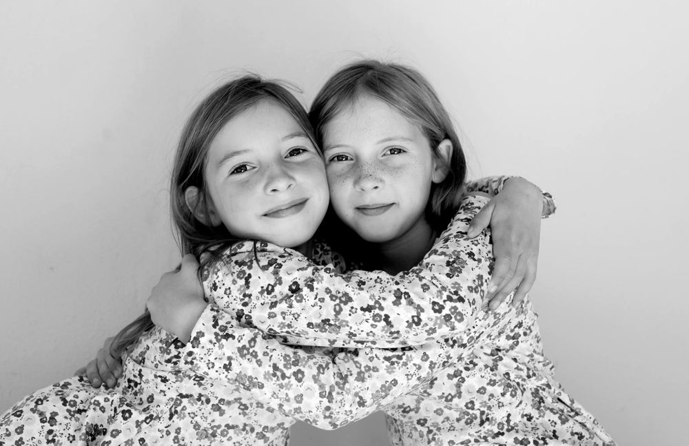 Black and white portrait of two children in floral dresses sitting close together and smiling warmly.