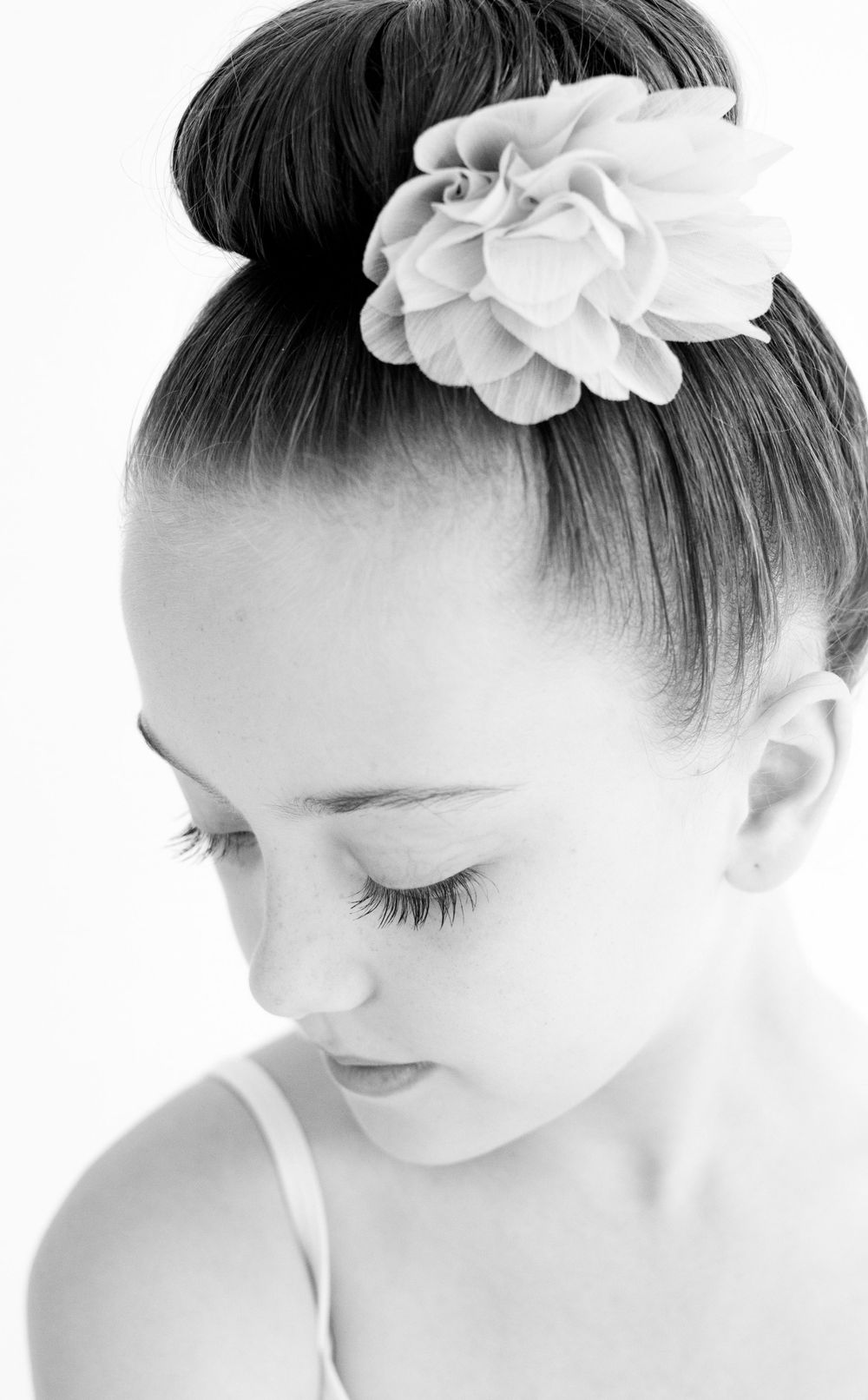 Close-up black and white profile of a ballet dancer with a white flower in her hair bun.