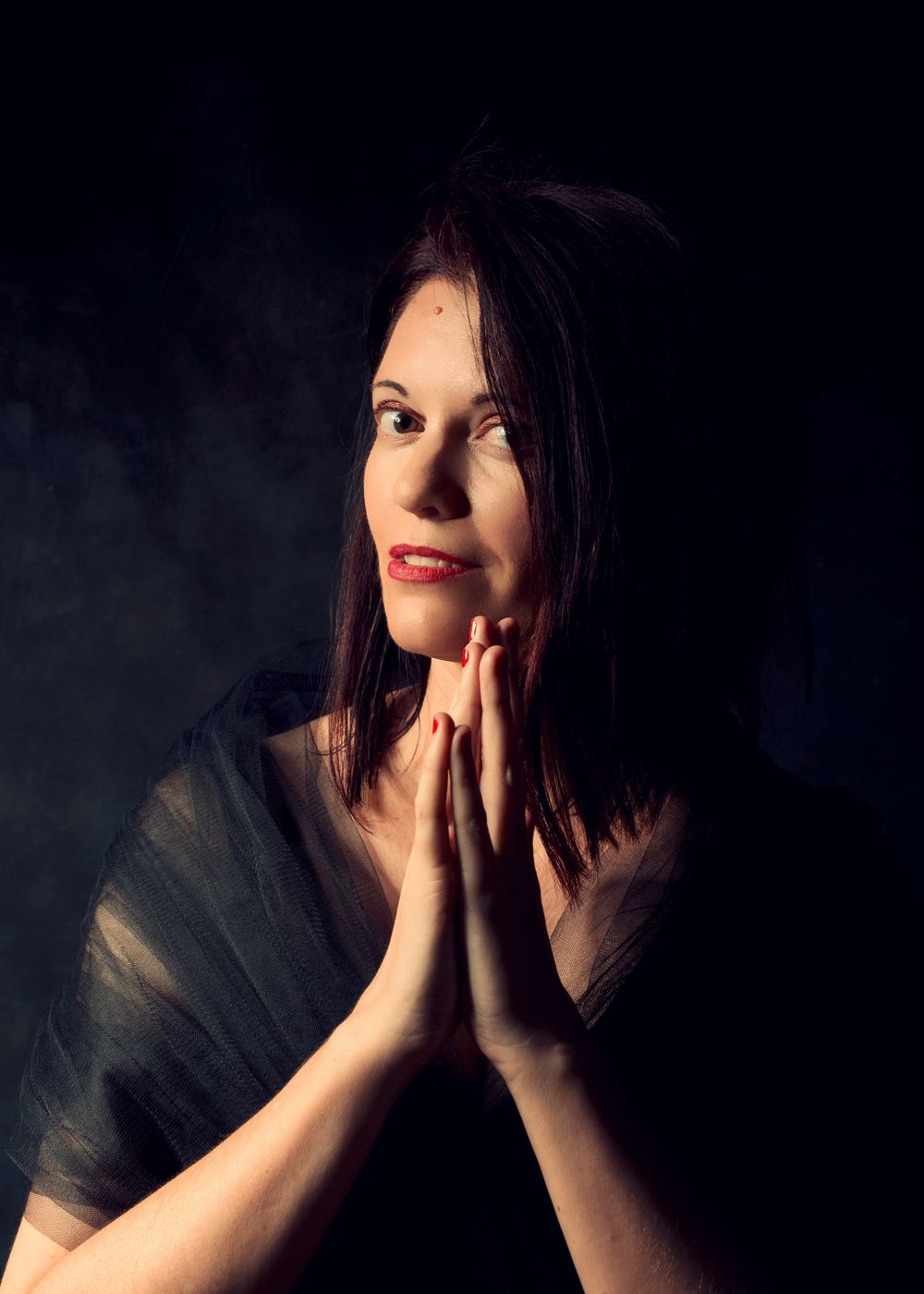 An atmospheric portrait of a person in prayer pose against a dark background with dramatic lighting.