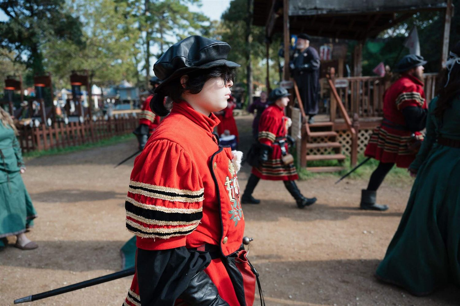 A performer in a red and black striped Renaissance costume walks through a festival ground.