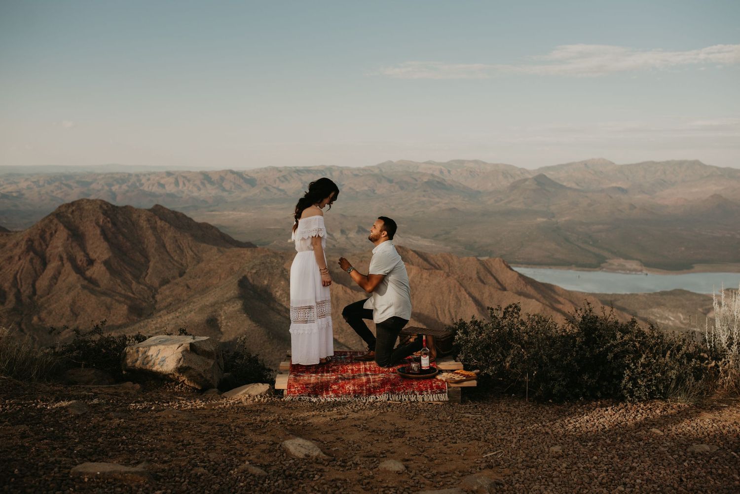 A couple sits together on a scenic mountain overlook during golden hour.