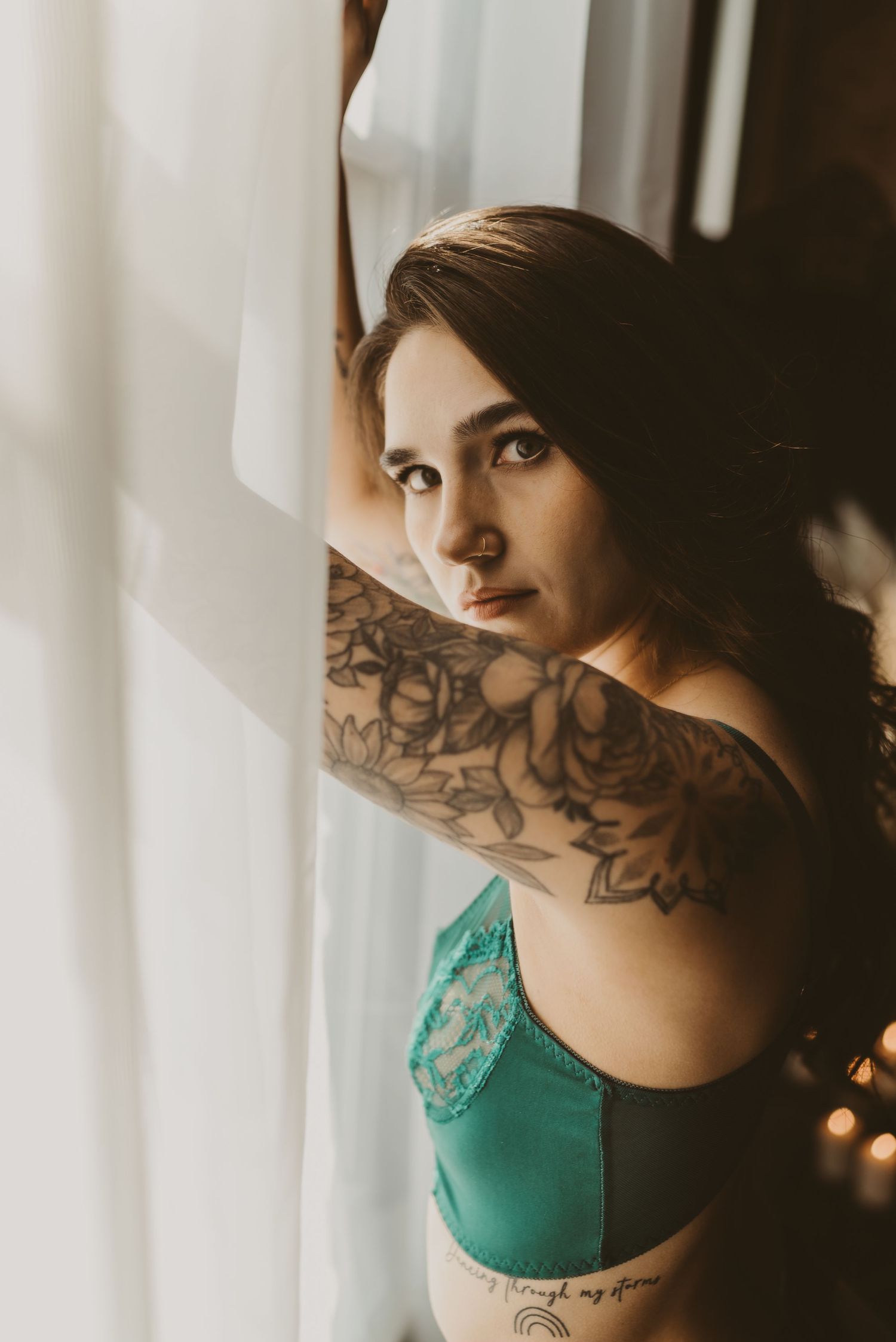 Artistic portrait by window showing floral arm tattoo and green lingerie.