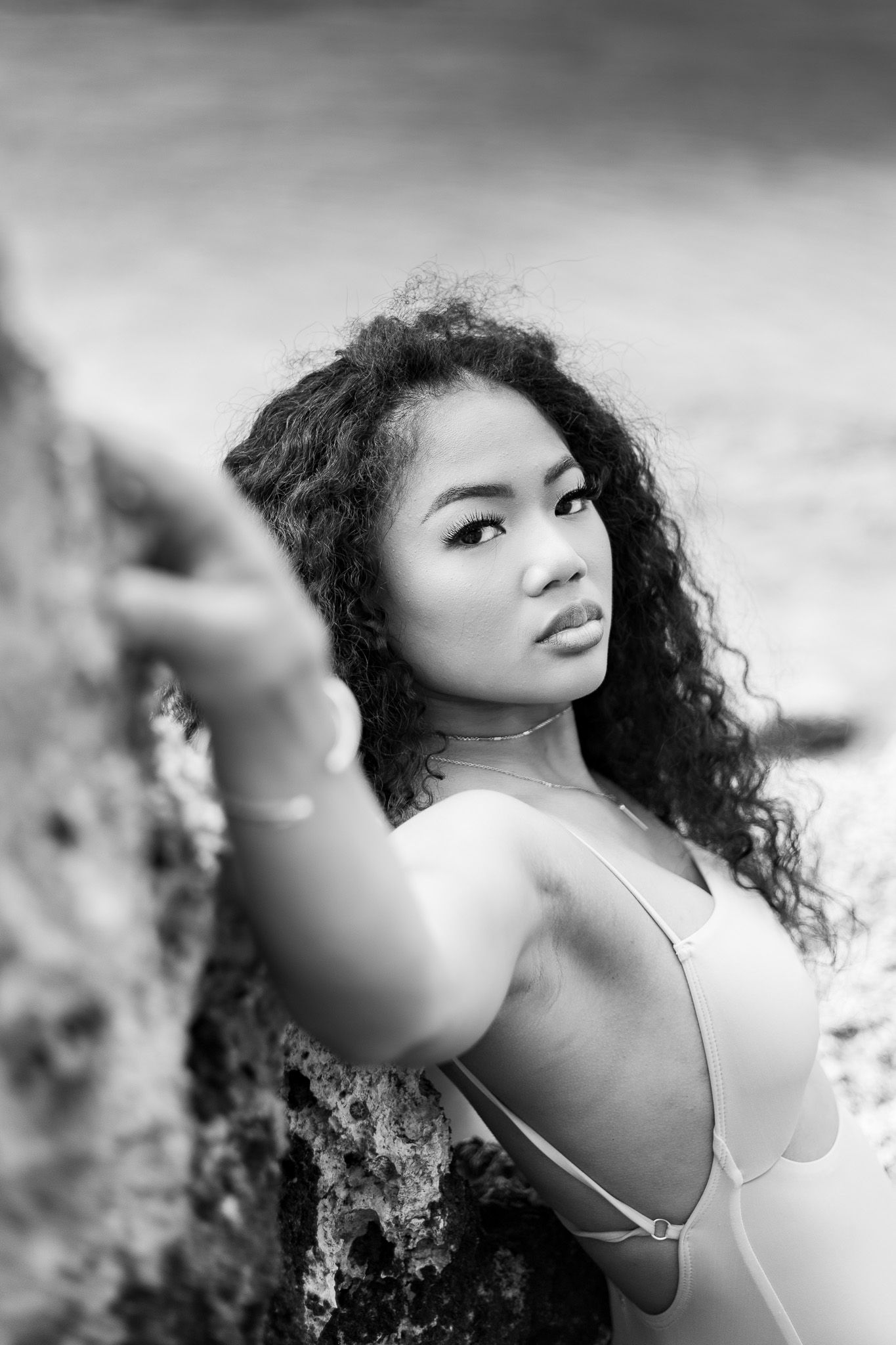 Black and white portrait of a person with curly hair posing against a rocky backdrop.