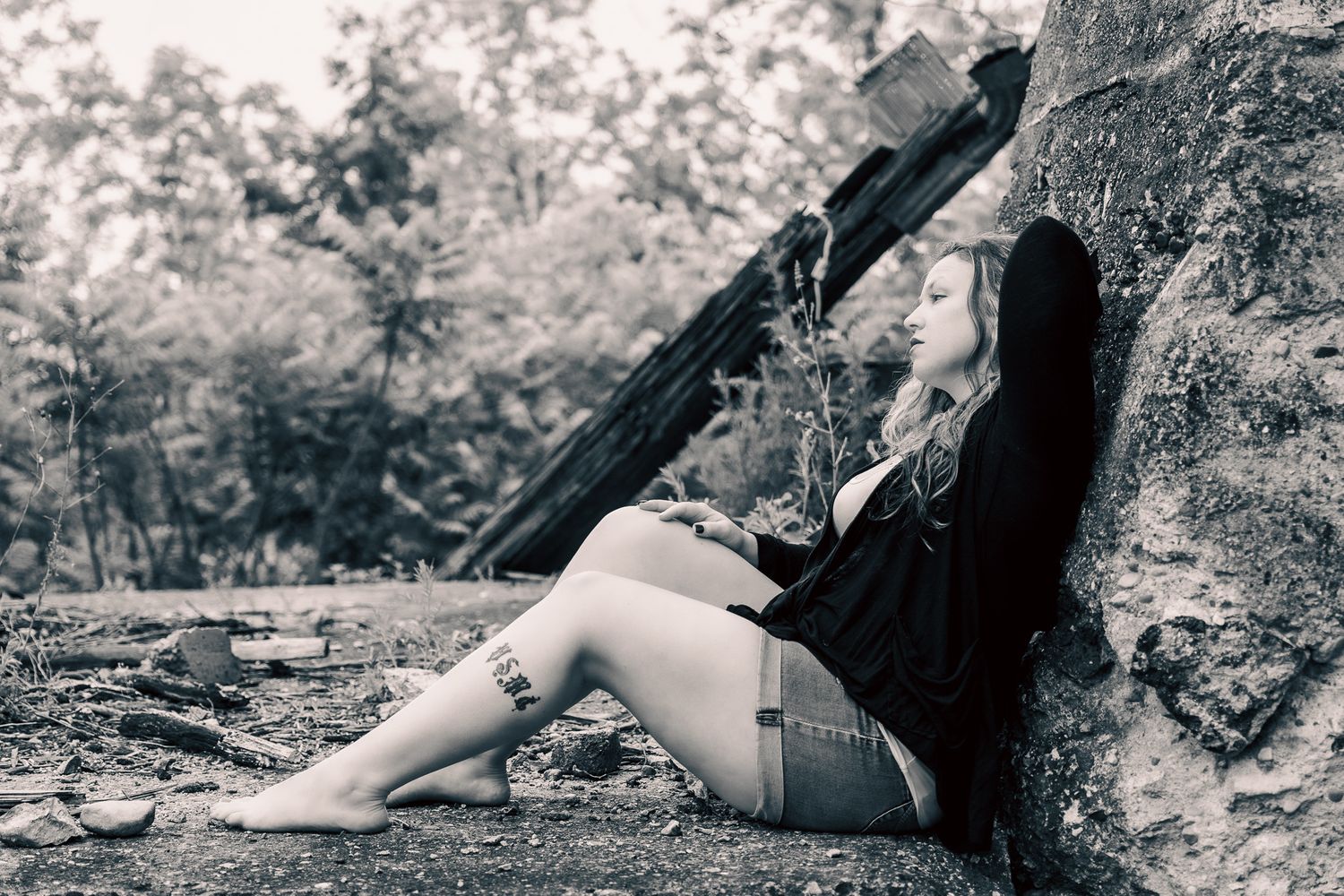 Artistic black and white photo of someone posing with camera equipment against rocks outdoors.