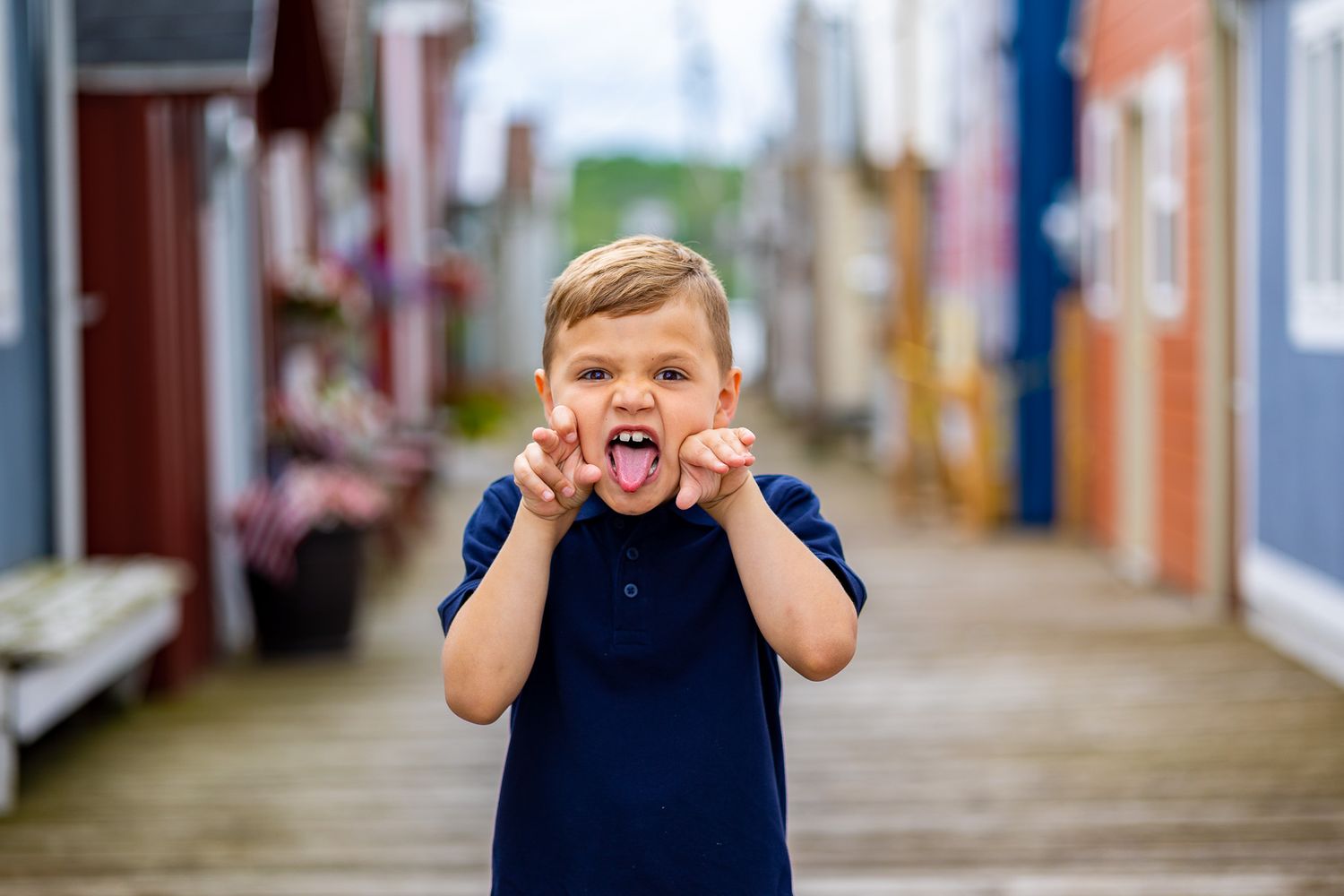A small child in a navy blue shirt expressing excitement on a wooden boardwalk.