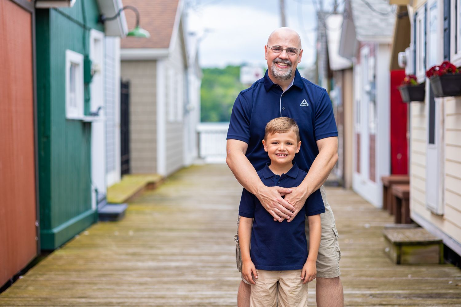 A parent and child wearing matching navy shirts pose together on a colorful boardwalk.
