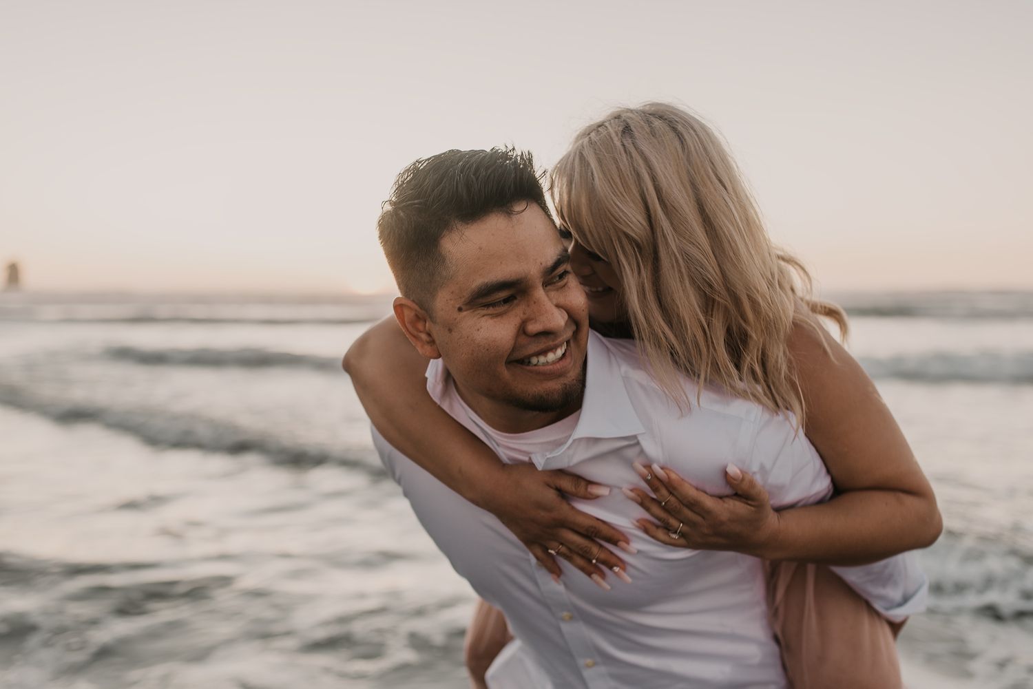 A romantic couple laughs and embraces on a beach at sunset.