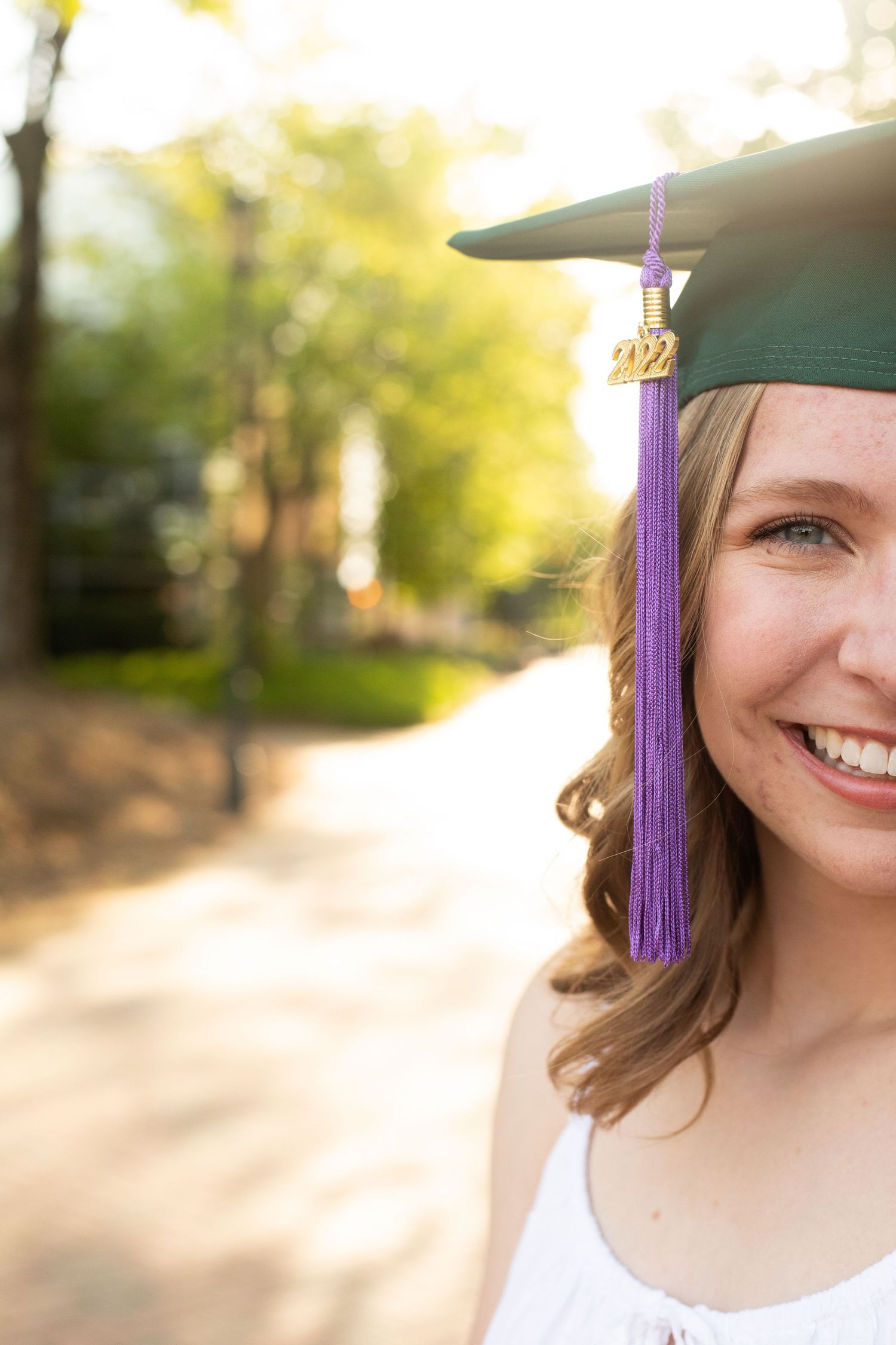 Close-up graduation portrait showing green cap with purple tassel against sunny background.
