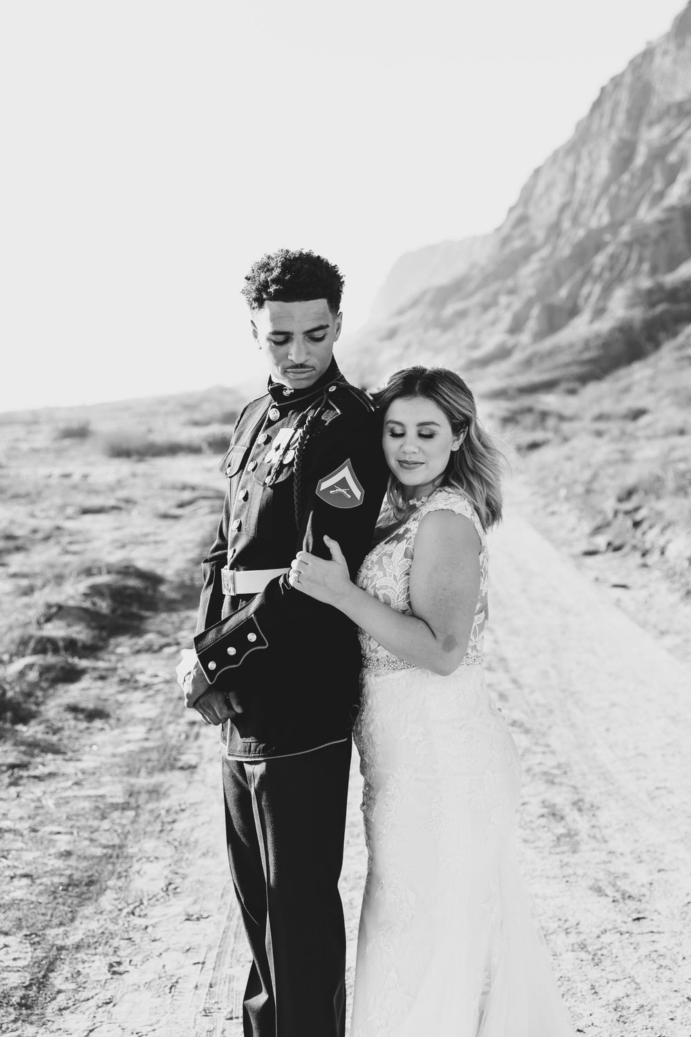 Black and white portrait of a military couple against dramatic desert cliffs.