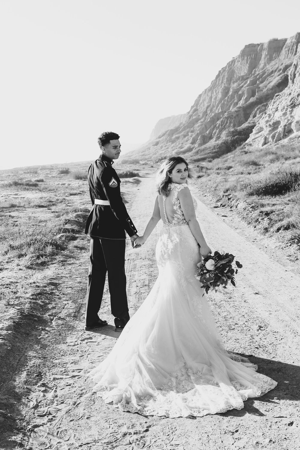 Black and white wedding photo of couple holding hands on mountain trail.