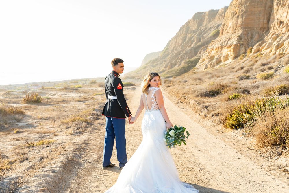 Wedding couple shares romantic moment on desert trail with towering cliffs behind them.