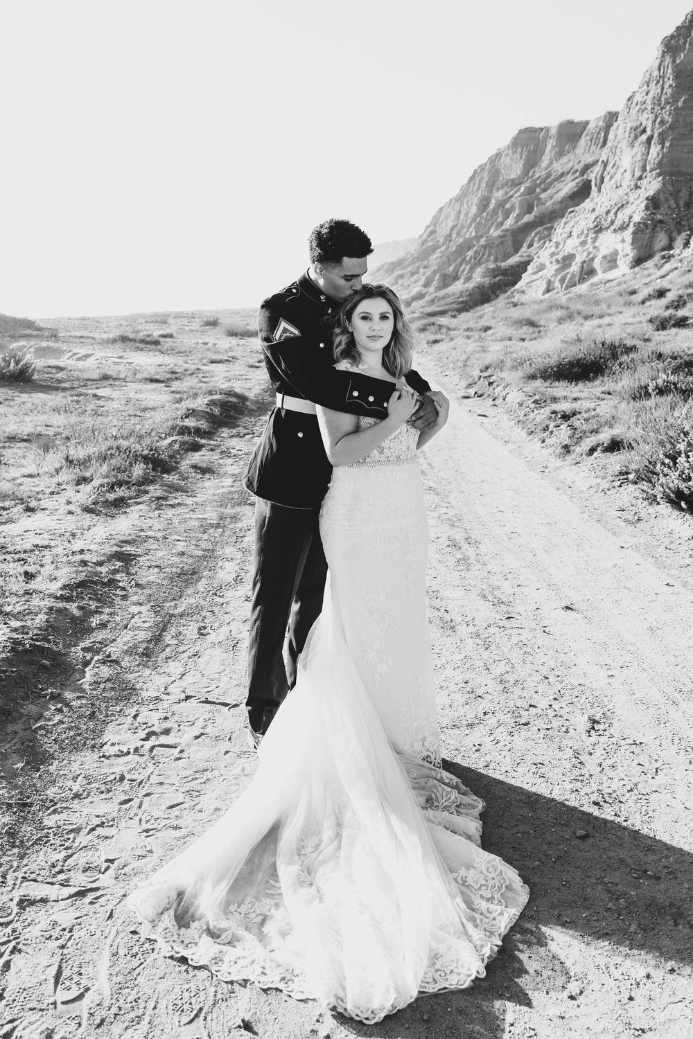 A black and white wedding photo shows a couple posing on a mountain path with dramatic cliffside scenery.