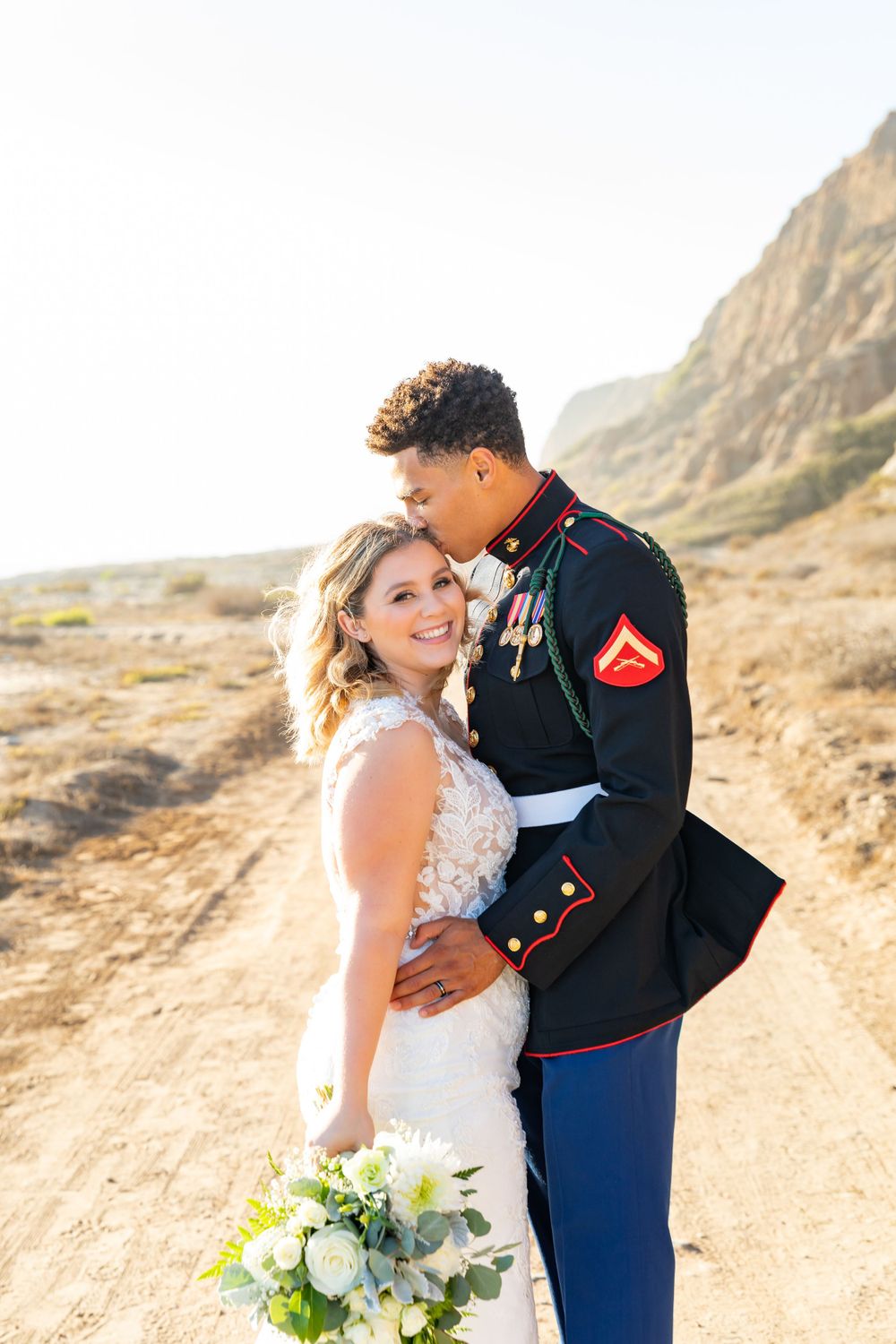 A tender moment between newlyweds on a scenic desert trail with mountains in the background.