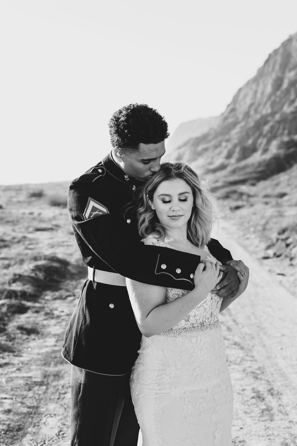A black and white portrait captures an intimate moment between newlyweds on a mountain path.
