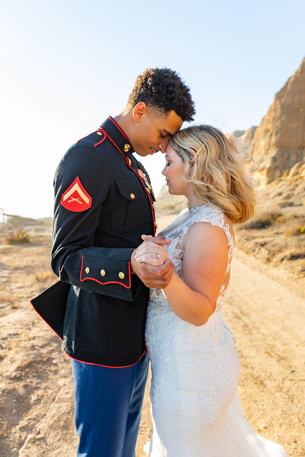 A Marine in dress blues shares a romantic moment with his bride on a desert trail.