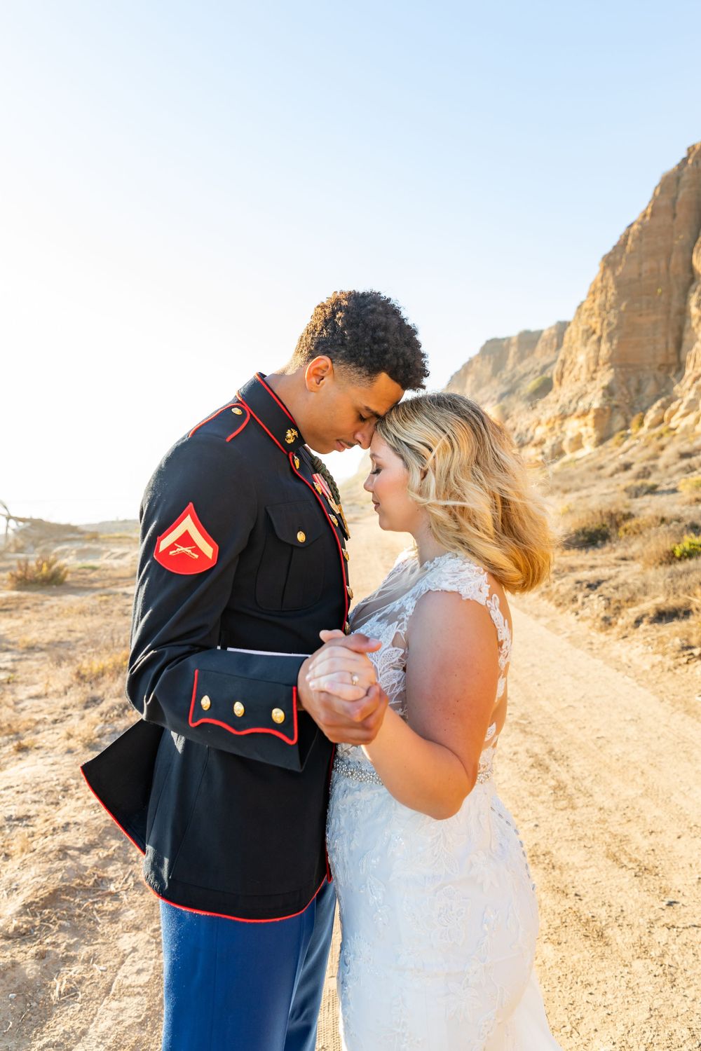 A military couple shares an intimate moment during their wedding photoshoot in a desert landscape.
